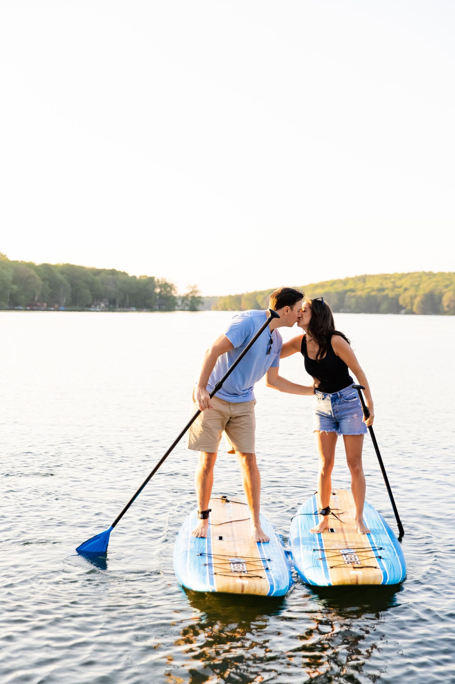 Couple sharing a romantic kiss while paddleboarding on a serene lake during sunset.
