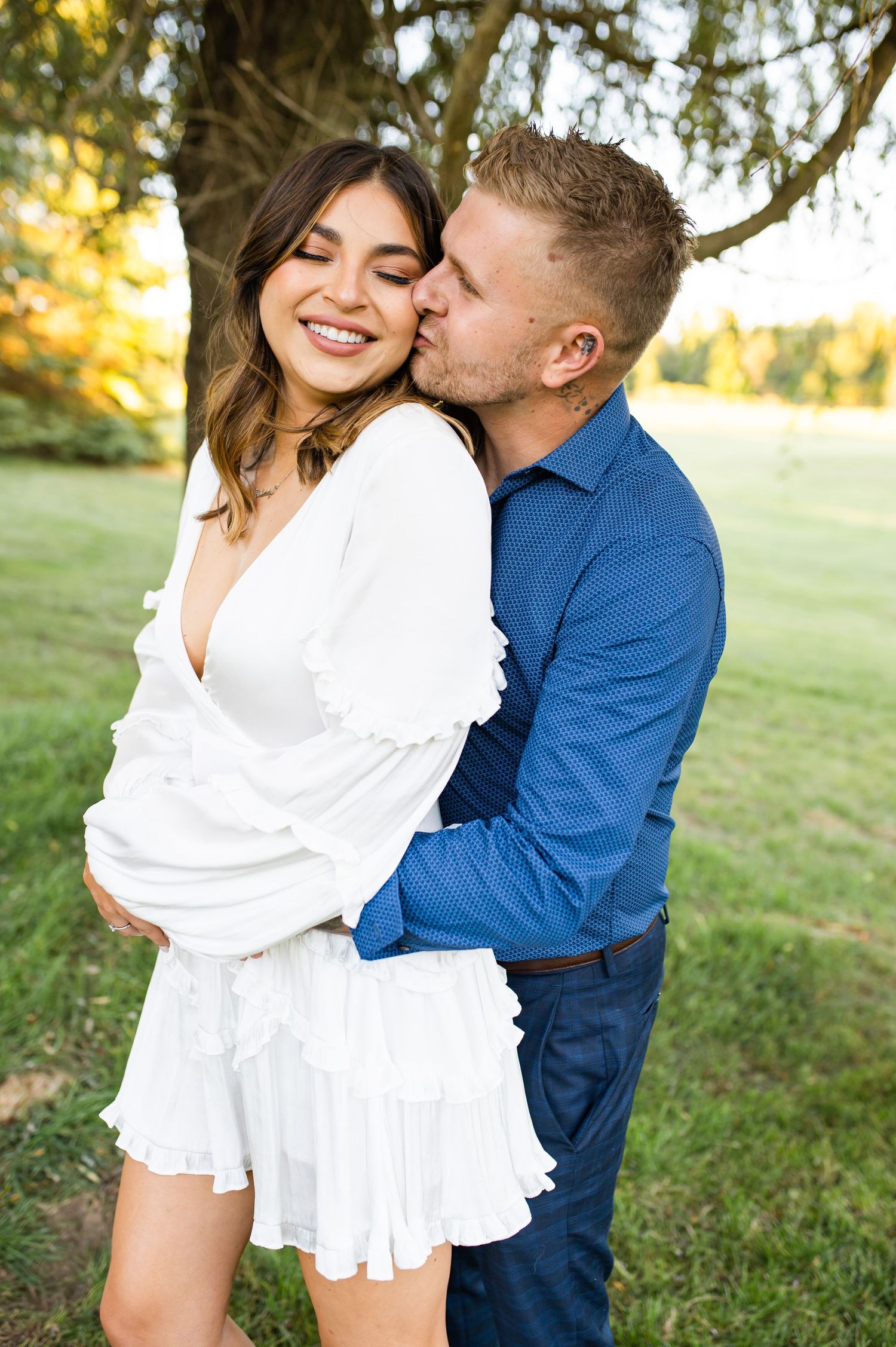 A playful couple laughs together during an outdoor photoshoot under a tree.