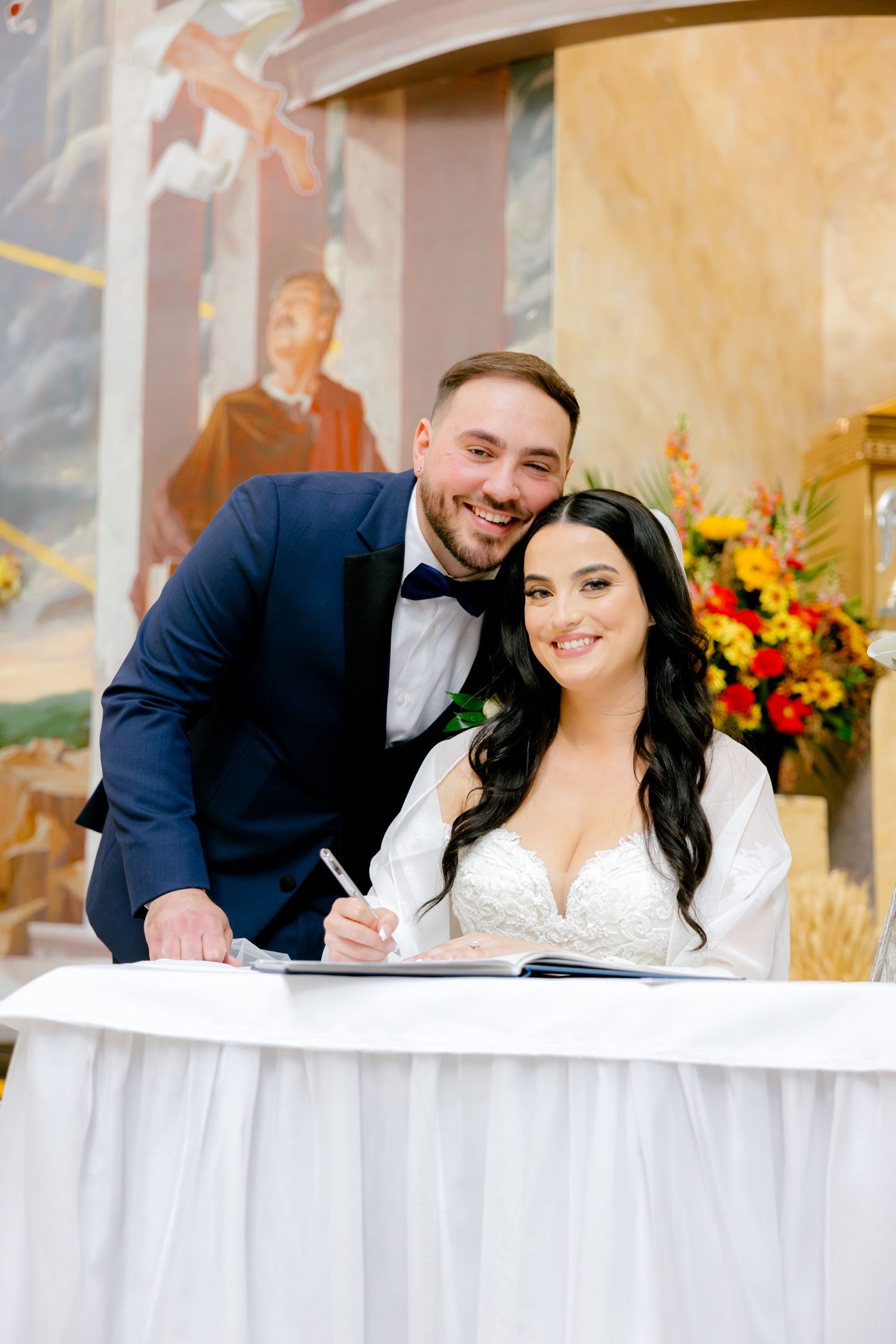 Couple signs wedding documents at a white-clothed table during their church ceremony.