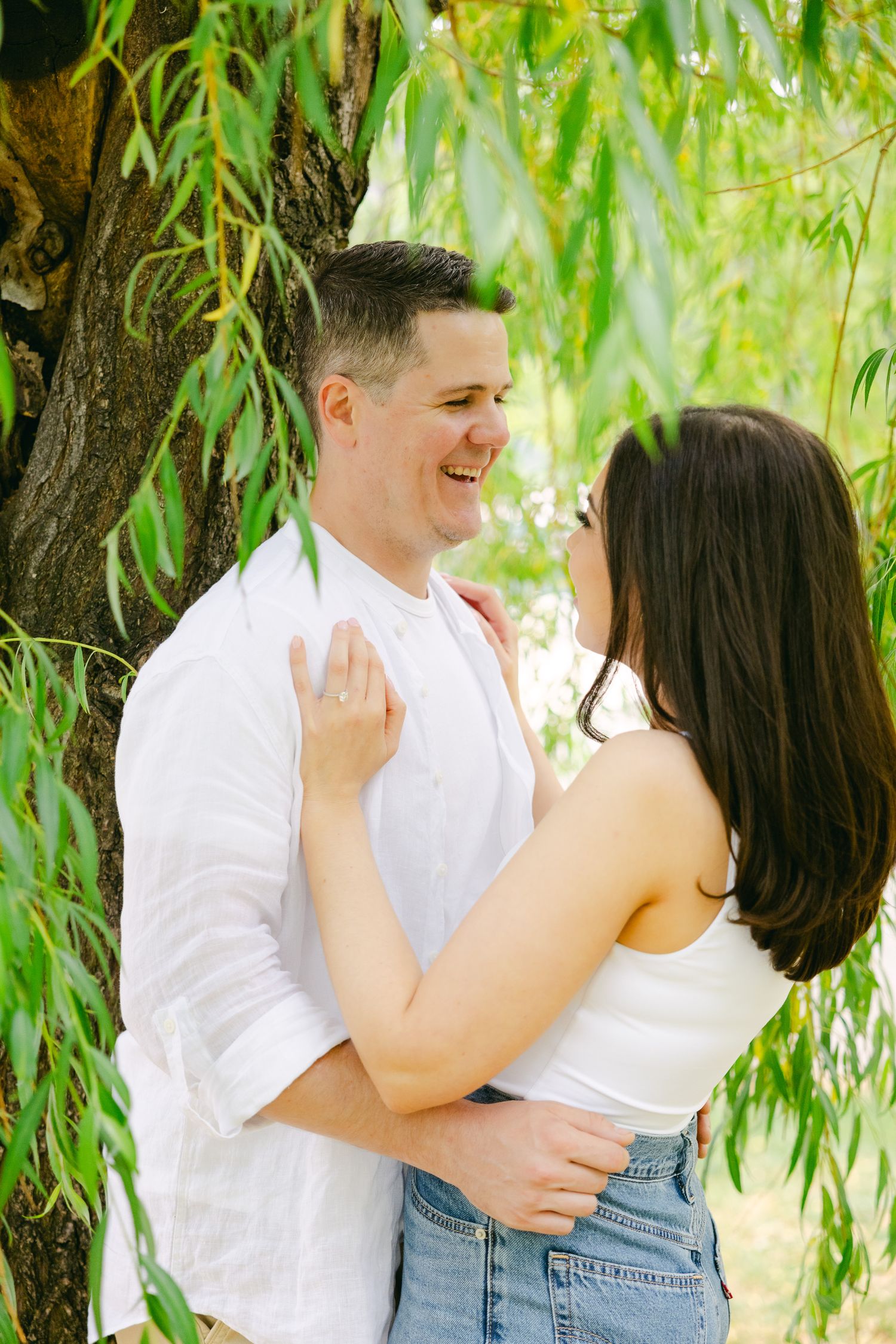 Happy couple sharing joyful moment beneath willow tree branches.