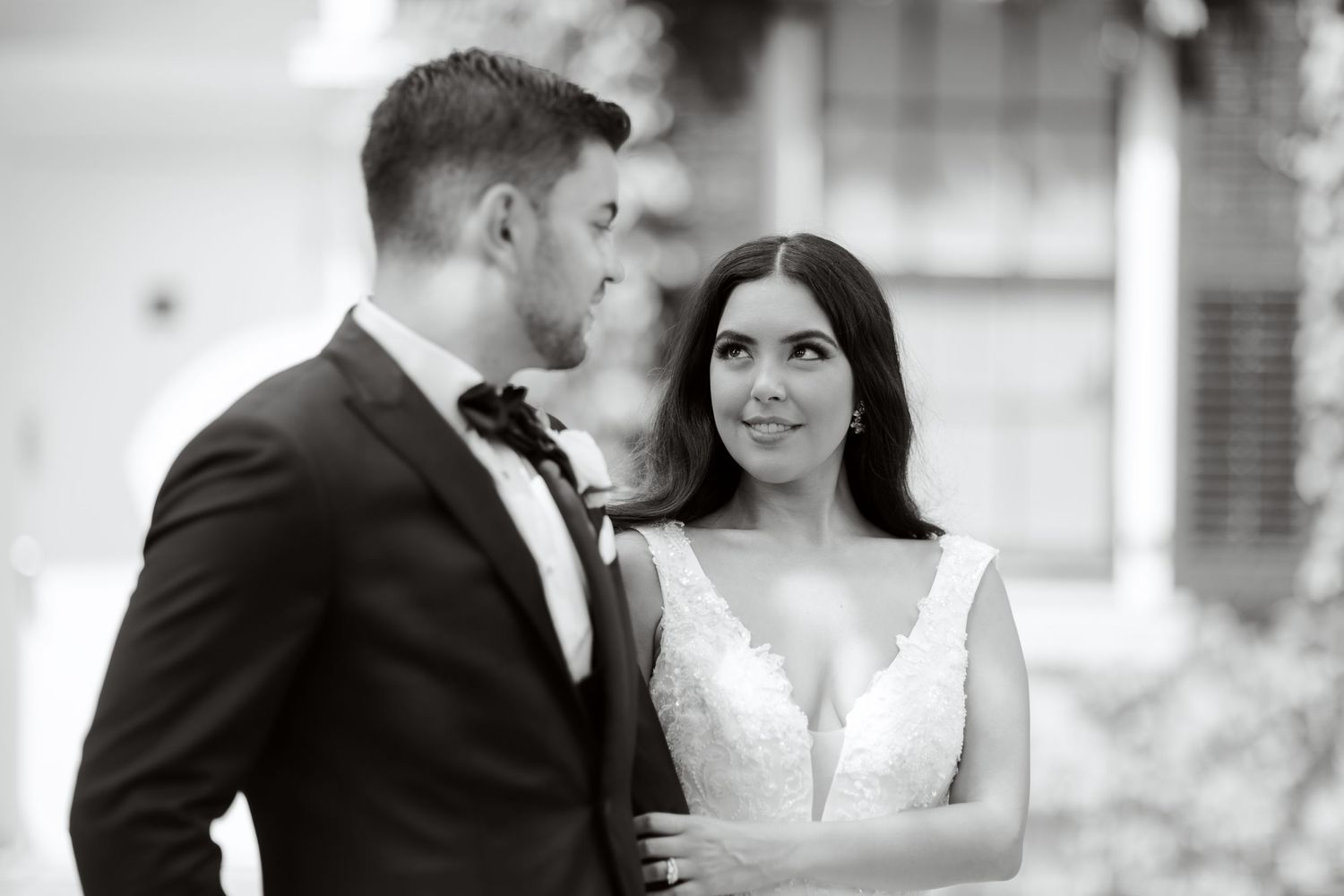 A romantic black and white wedding portrait of a couple in formal attire gazing at each other outdoors.