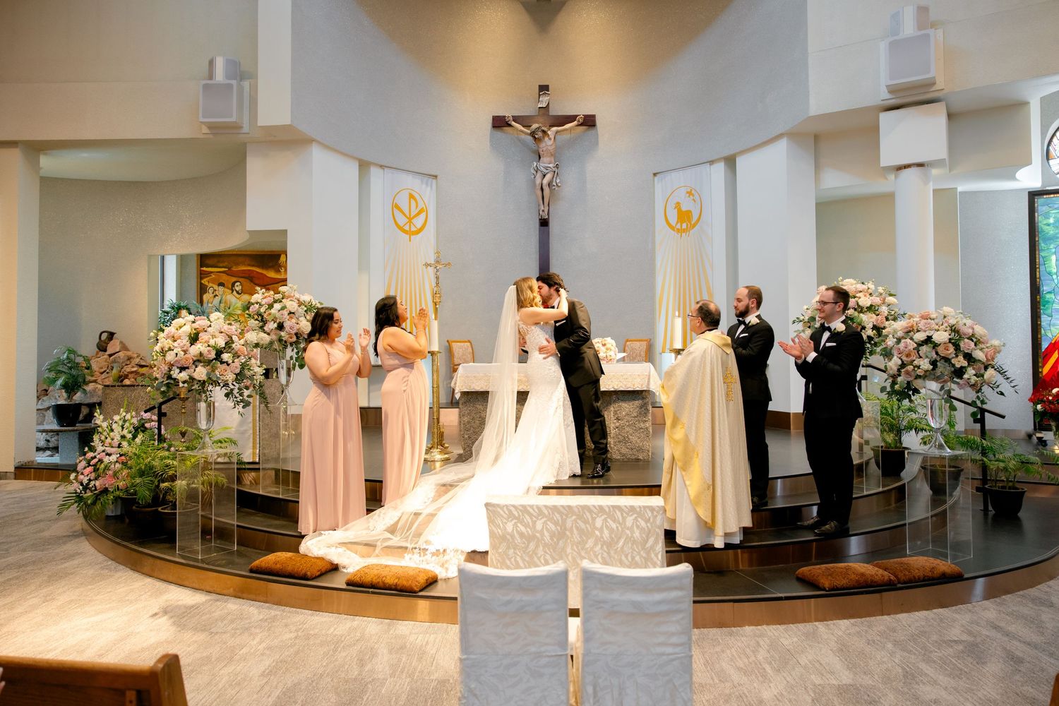 Wedding ceremony with floral arrangements and gold banners in modern church sanctuary.