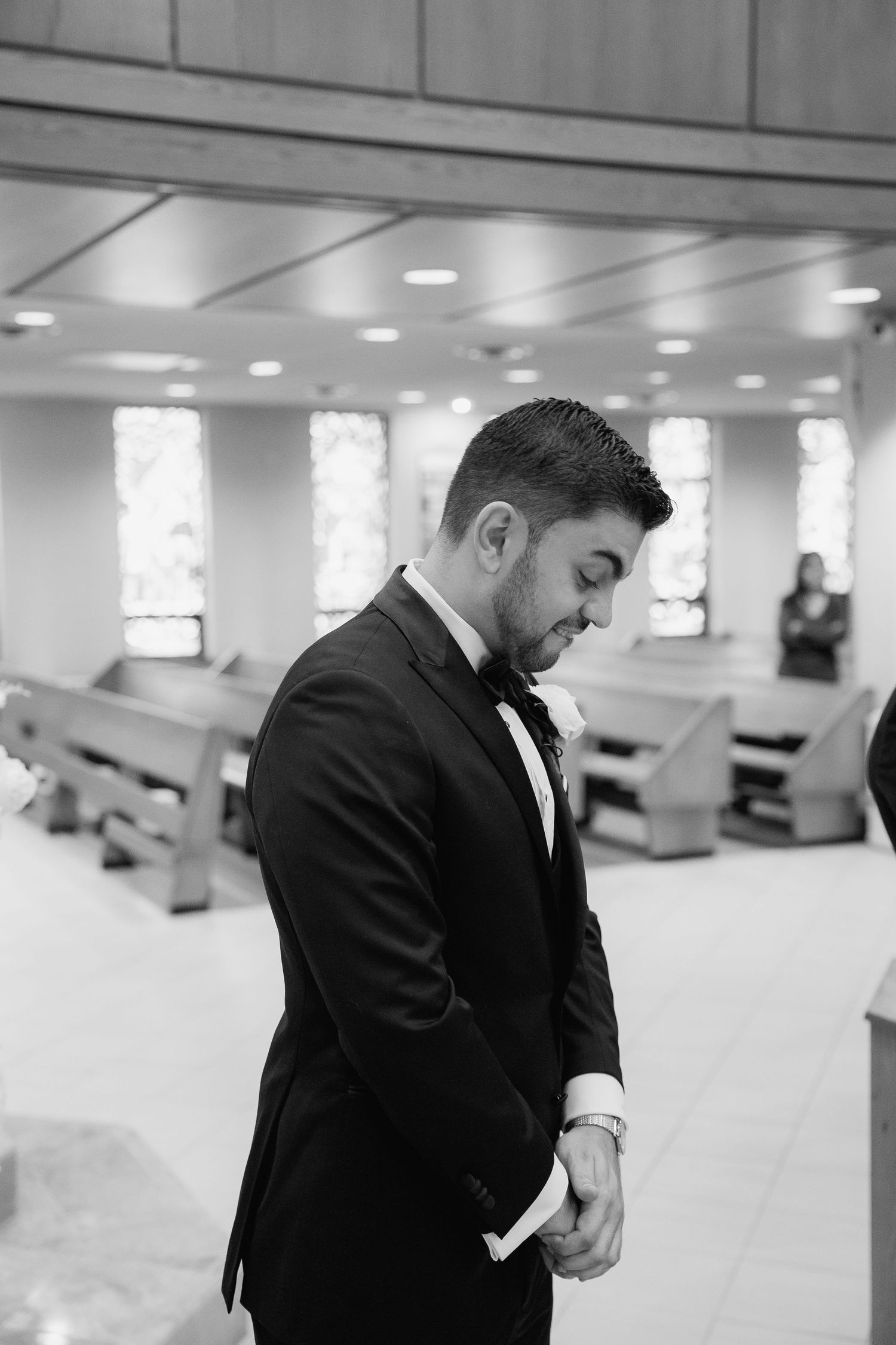 Black and white portrait of groom in formal attire looking down in church setting.
