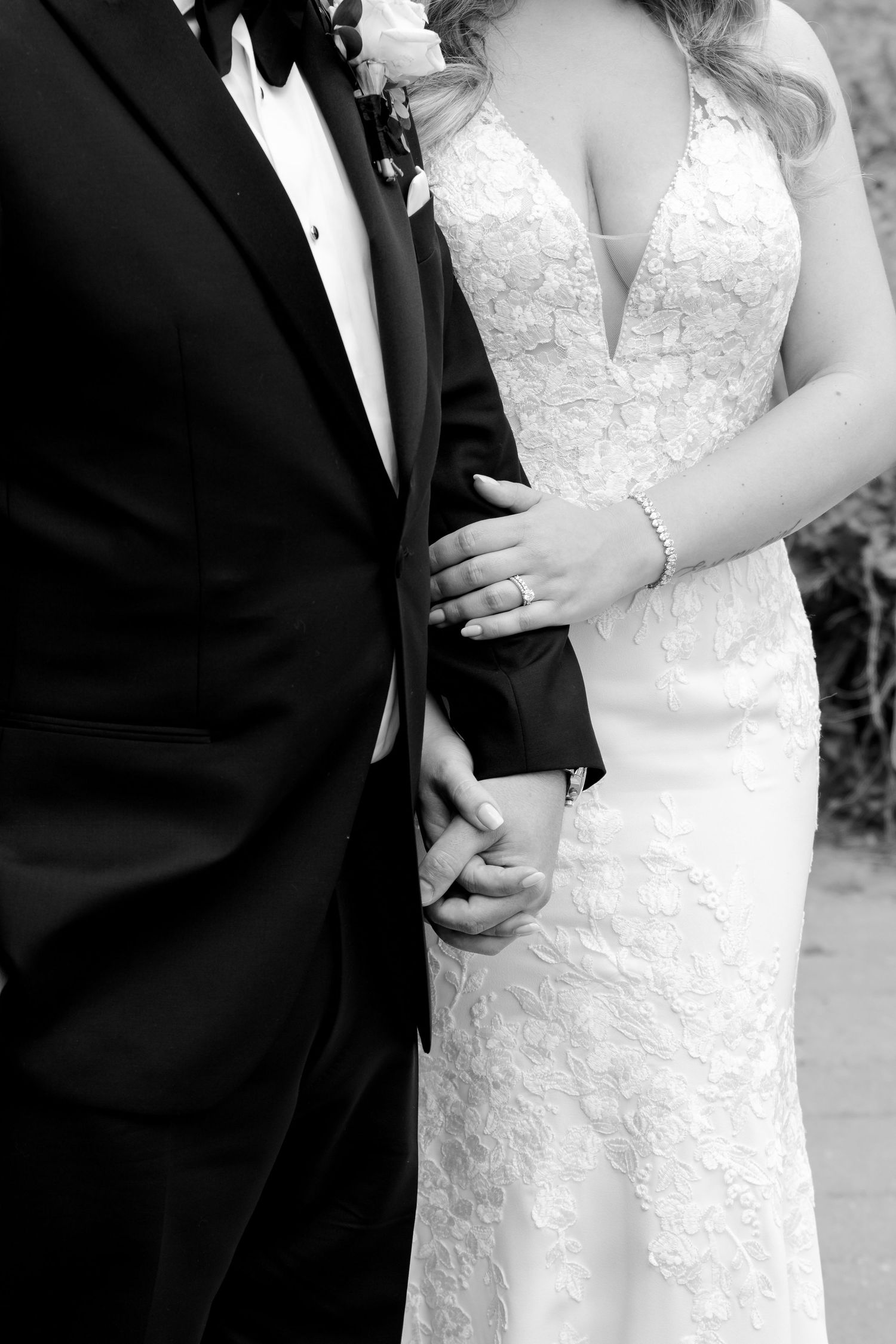 Close-up black and white detail of bride's lace dress and groom's tuxedo.