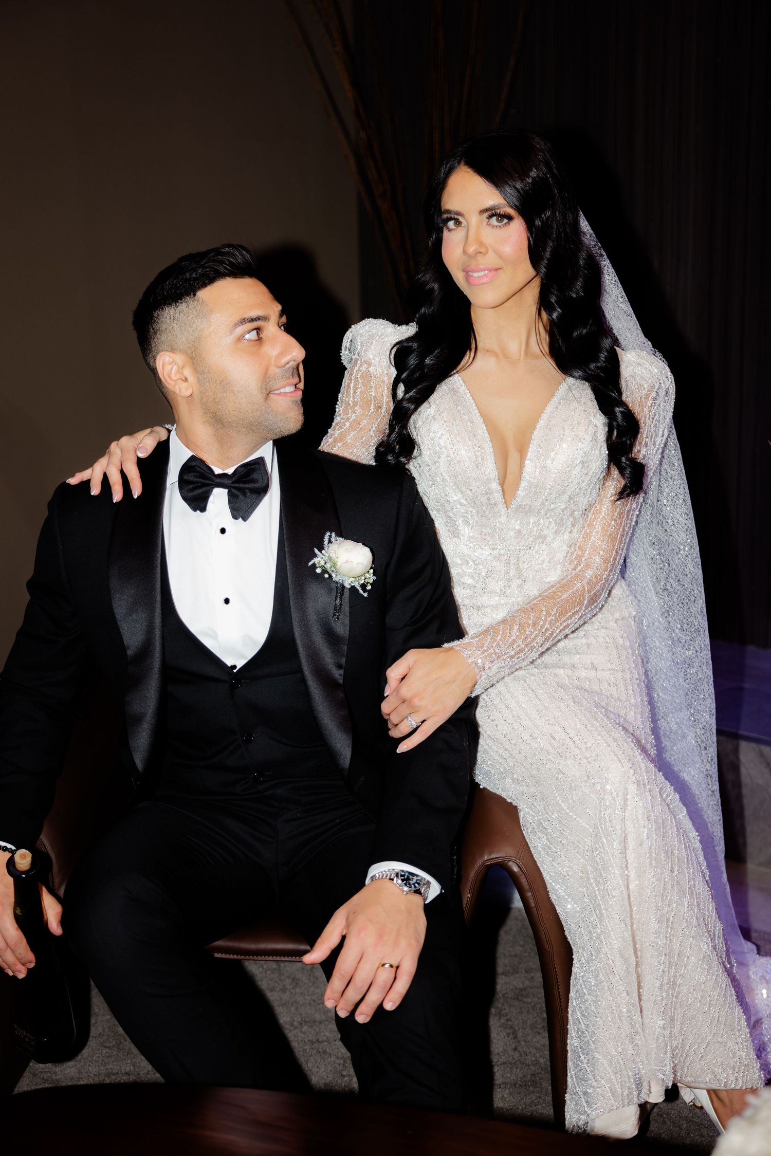 Bride in lace gown poses with groom in tuxedo during elegant wedding photo session.