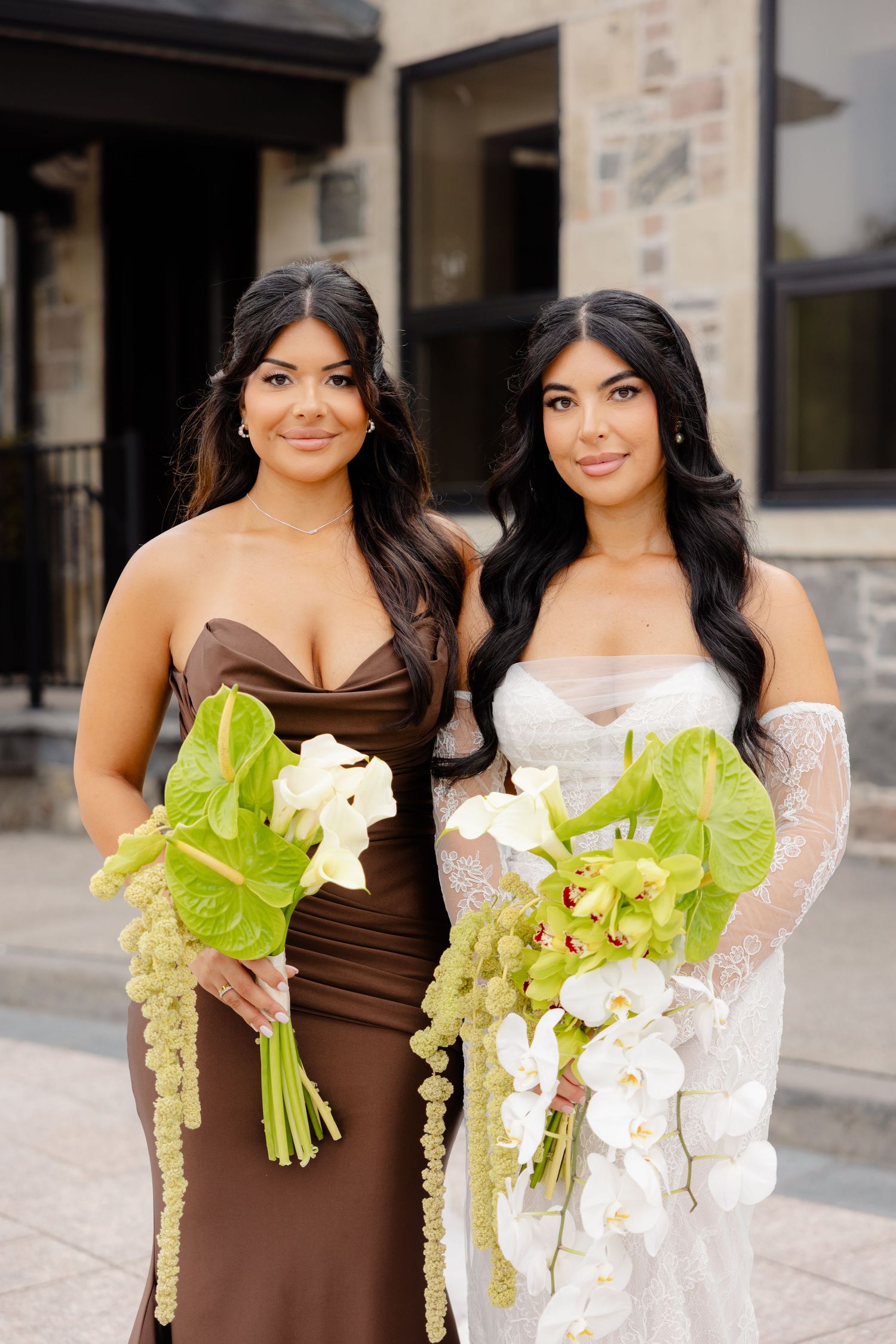 Two women in evening gowns pose with elegant white floral and green leaf bouquets for formal portraits.