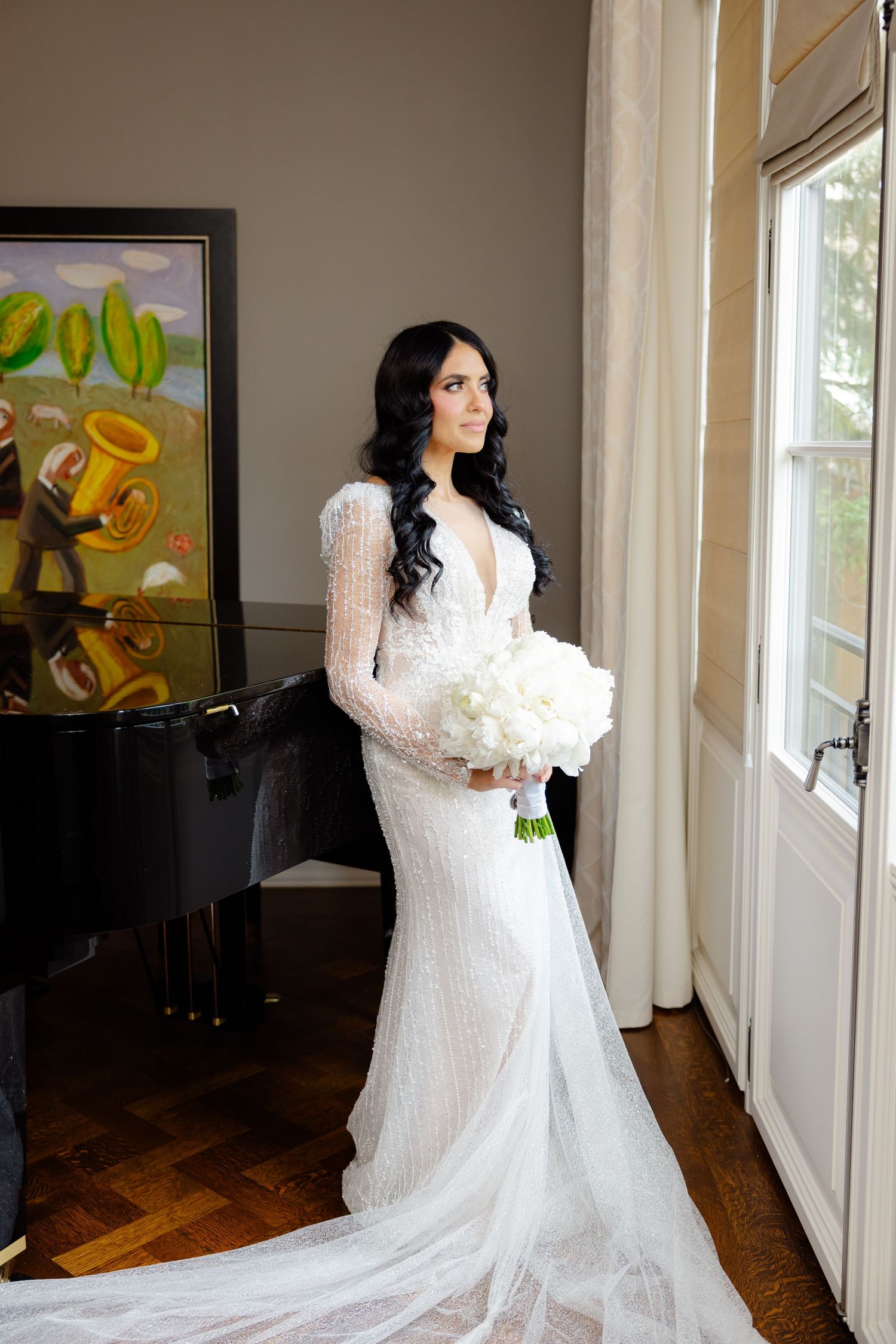 Long sleeve lace wedding gown with flowing train photographed by window.