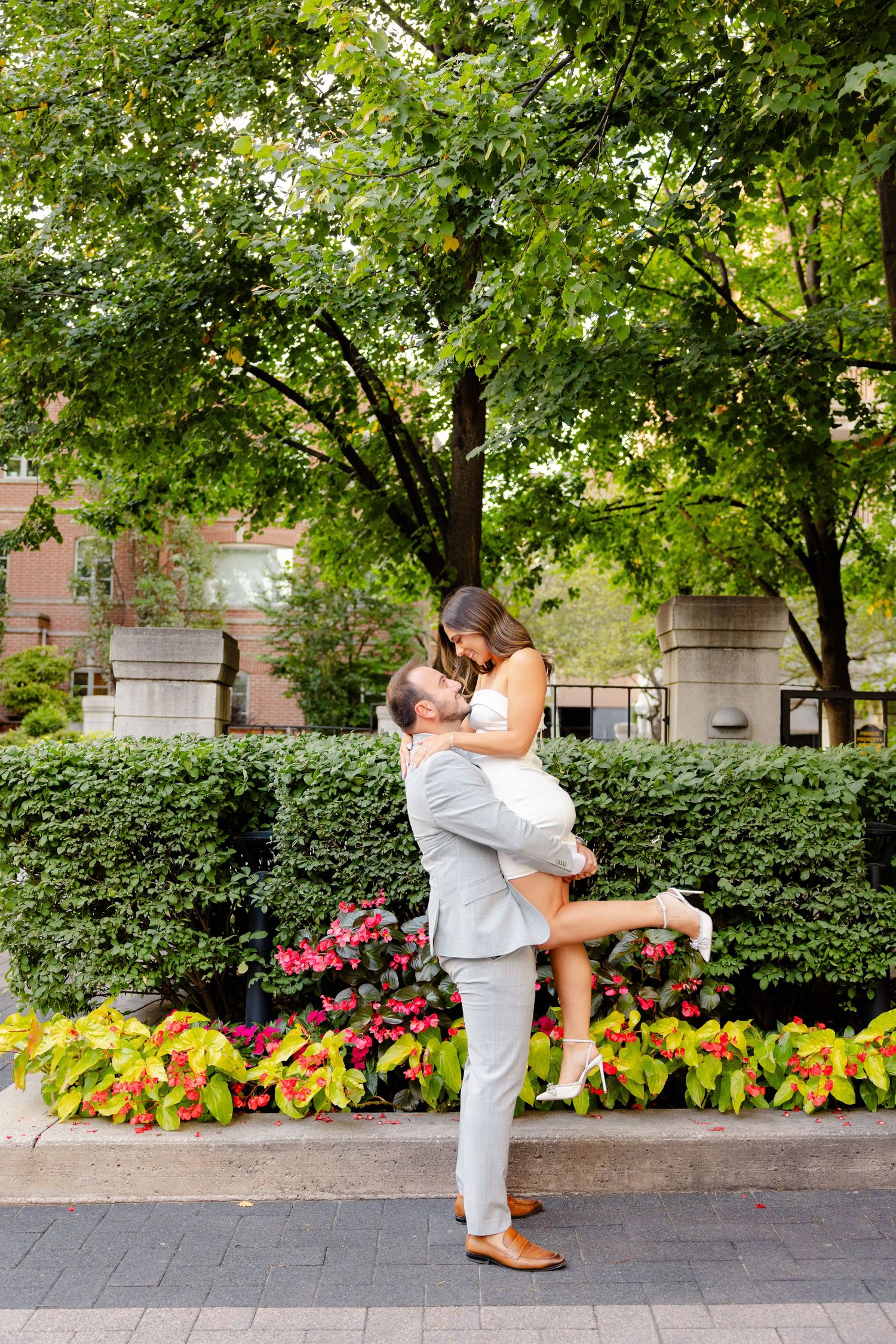 A romantic lift pose captured in front of a garden backdrop with colorful flowers.