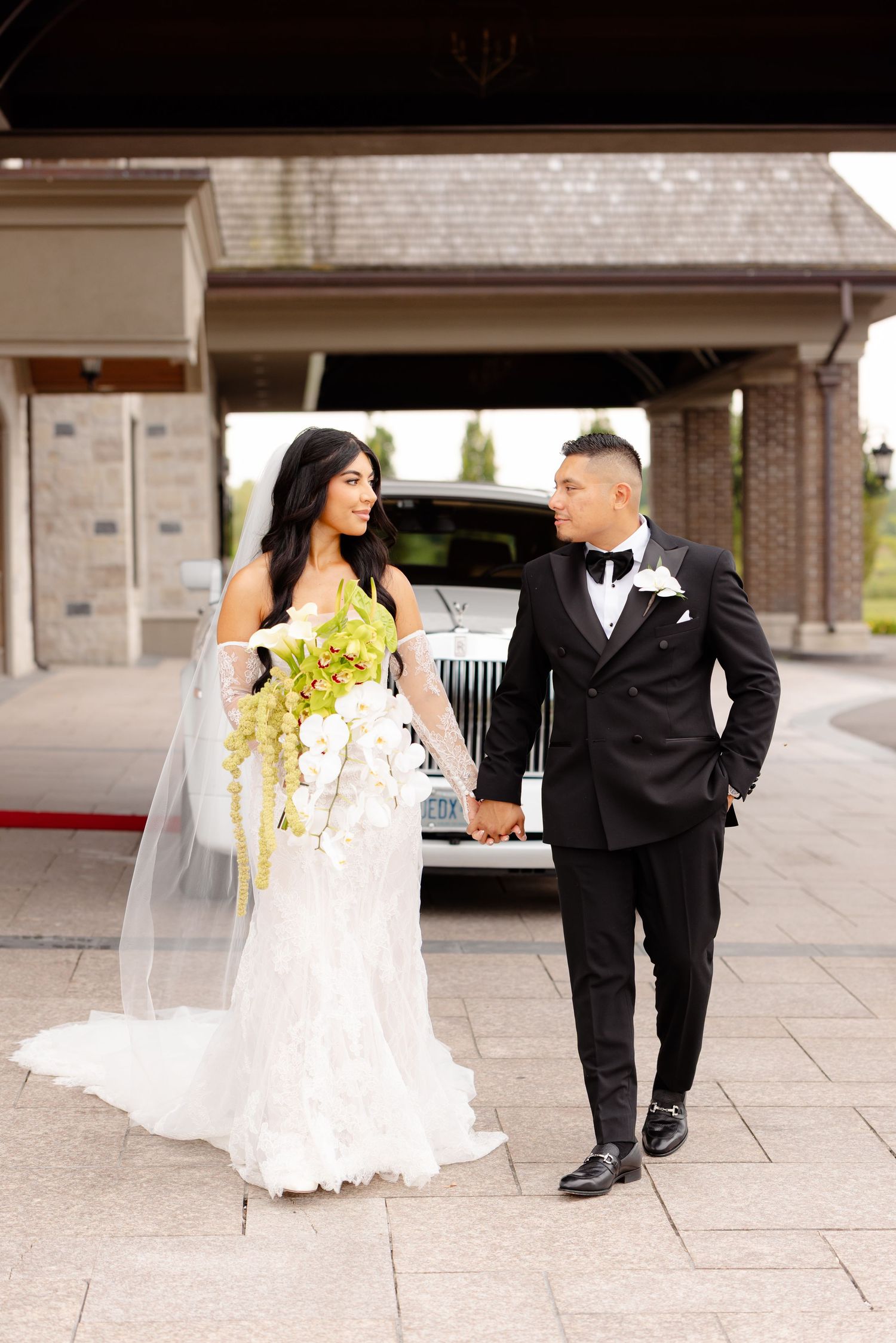 Wedding couple walking together on stone pavement in formal attire with flowing white dress and dark suit.