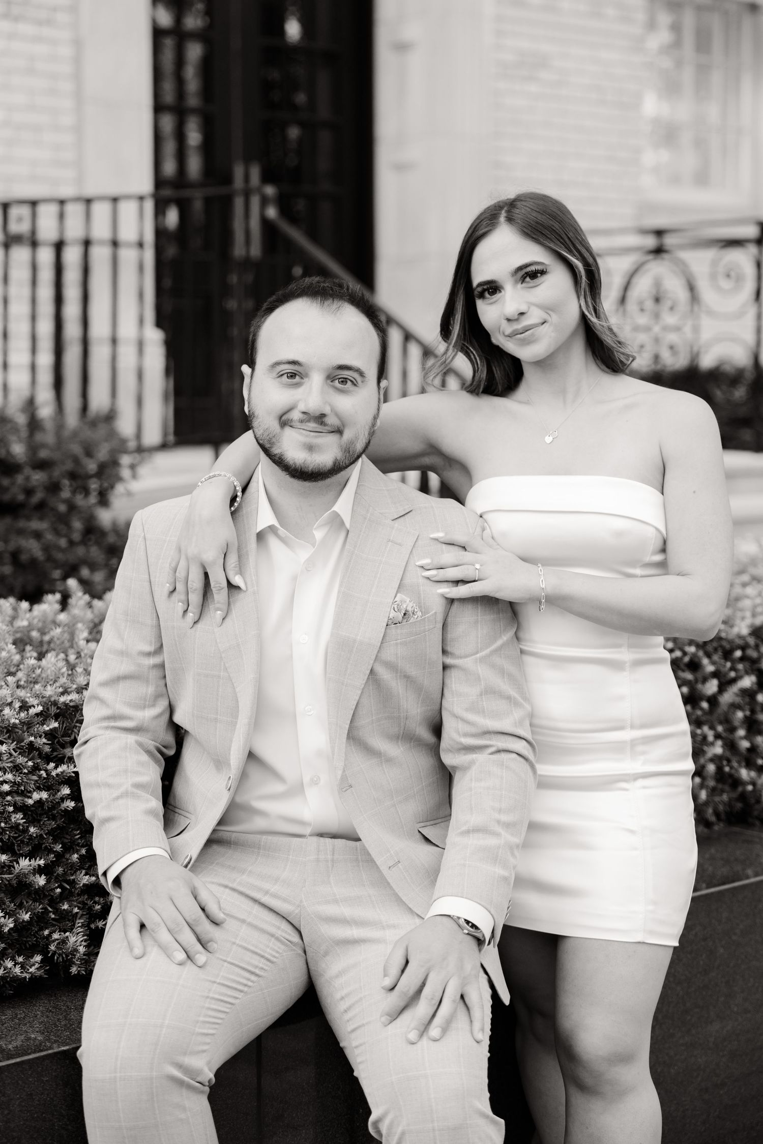 Black and white portrait of a couple in formal attire seated outside Chanel boutique.