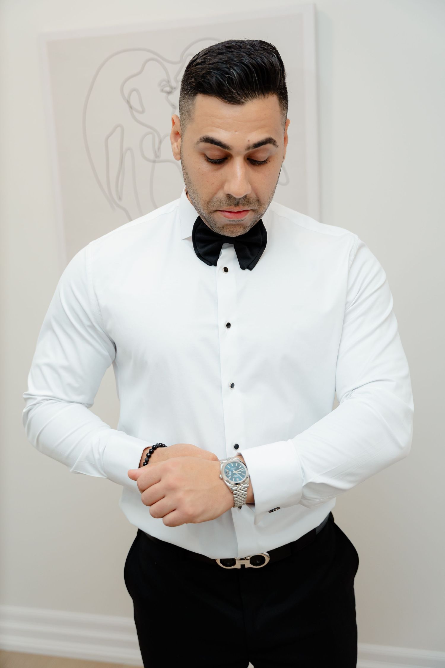 Dapper groomsman in white dress shirt and black bow tie checking his watch.