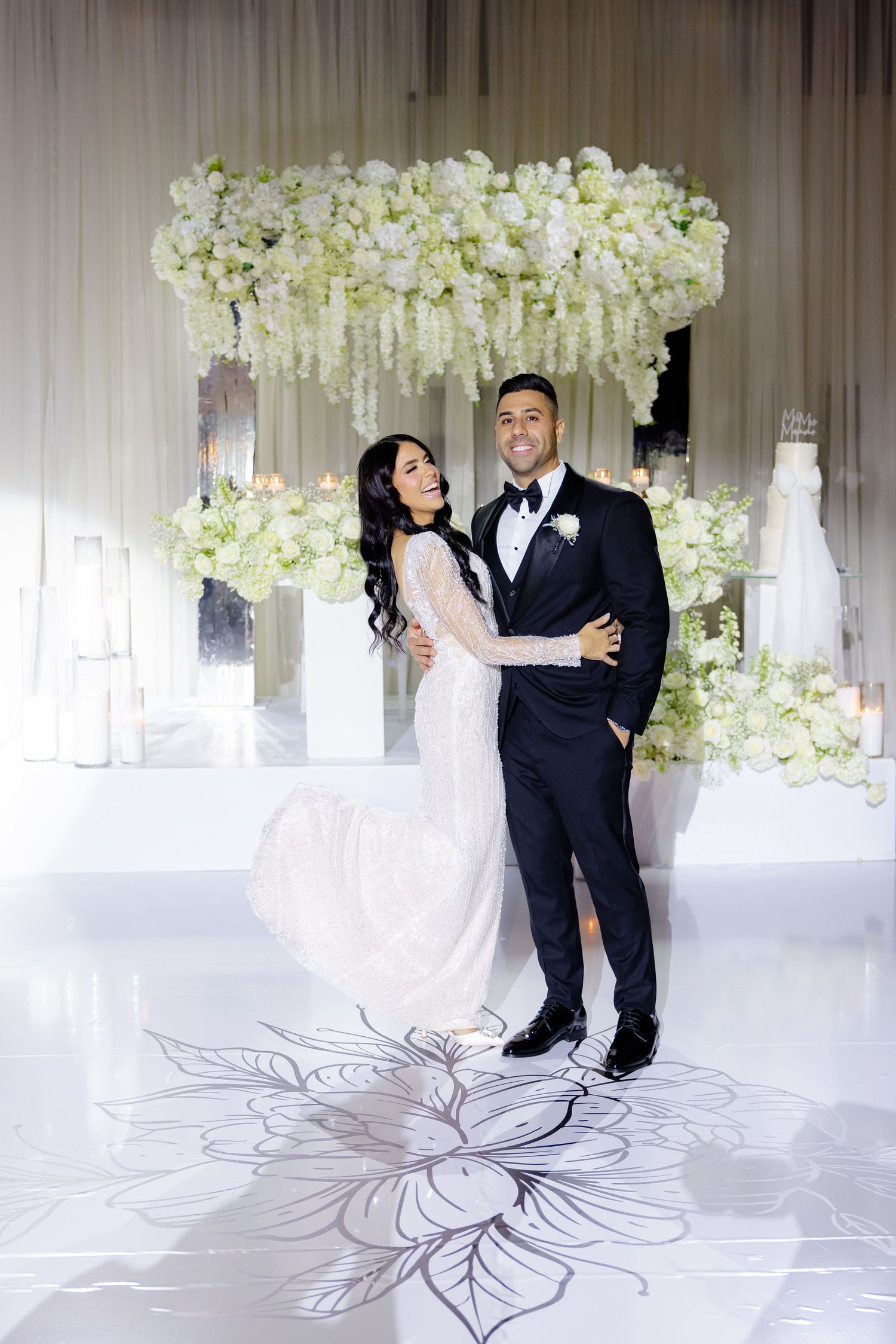 Wedding couple posing beneath a stunning white floral installation in their formal attire.