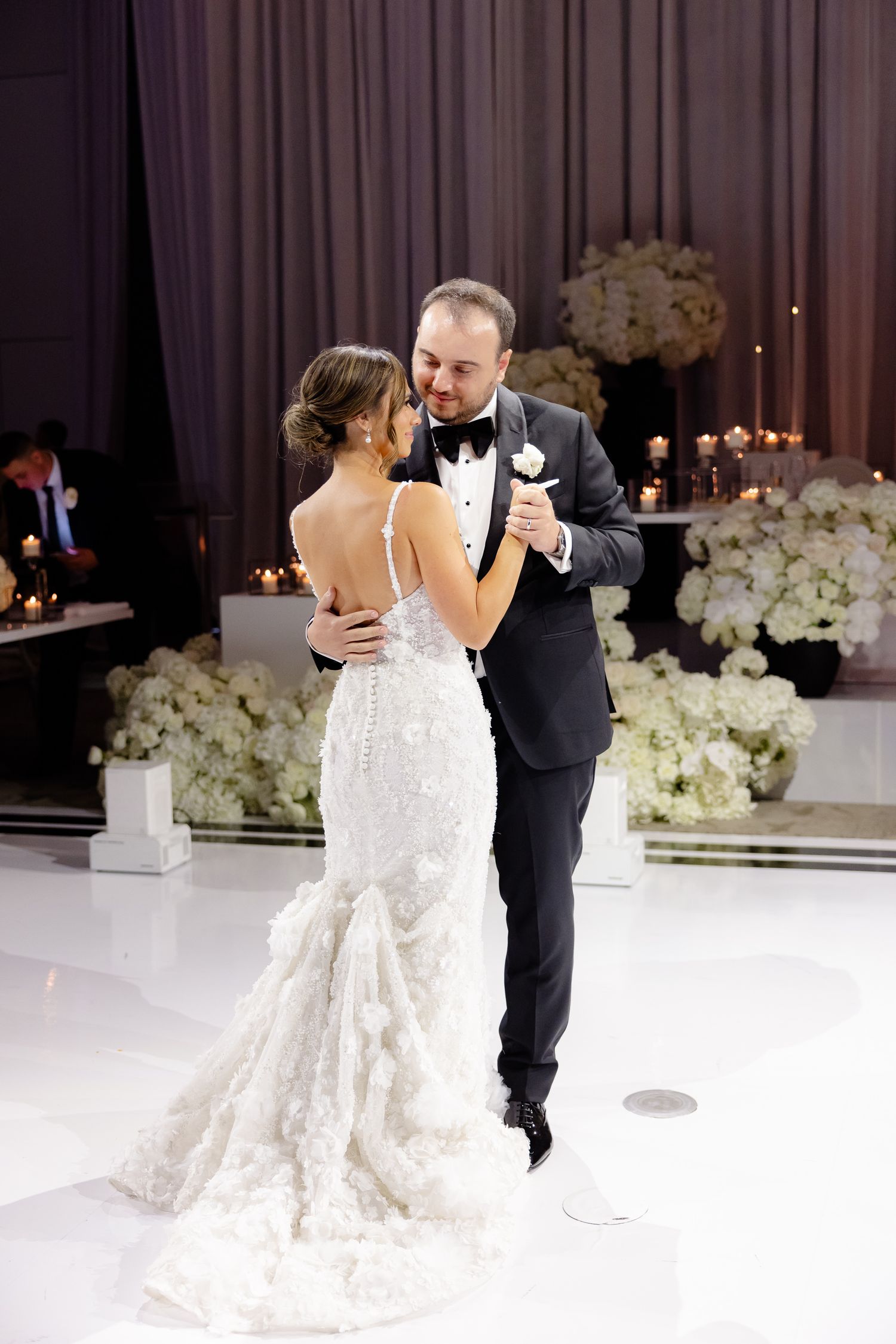 A couple shares their first dance at an elegant wedding reception with white floral decorations and candlelight.