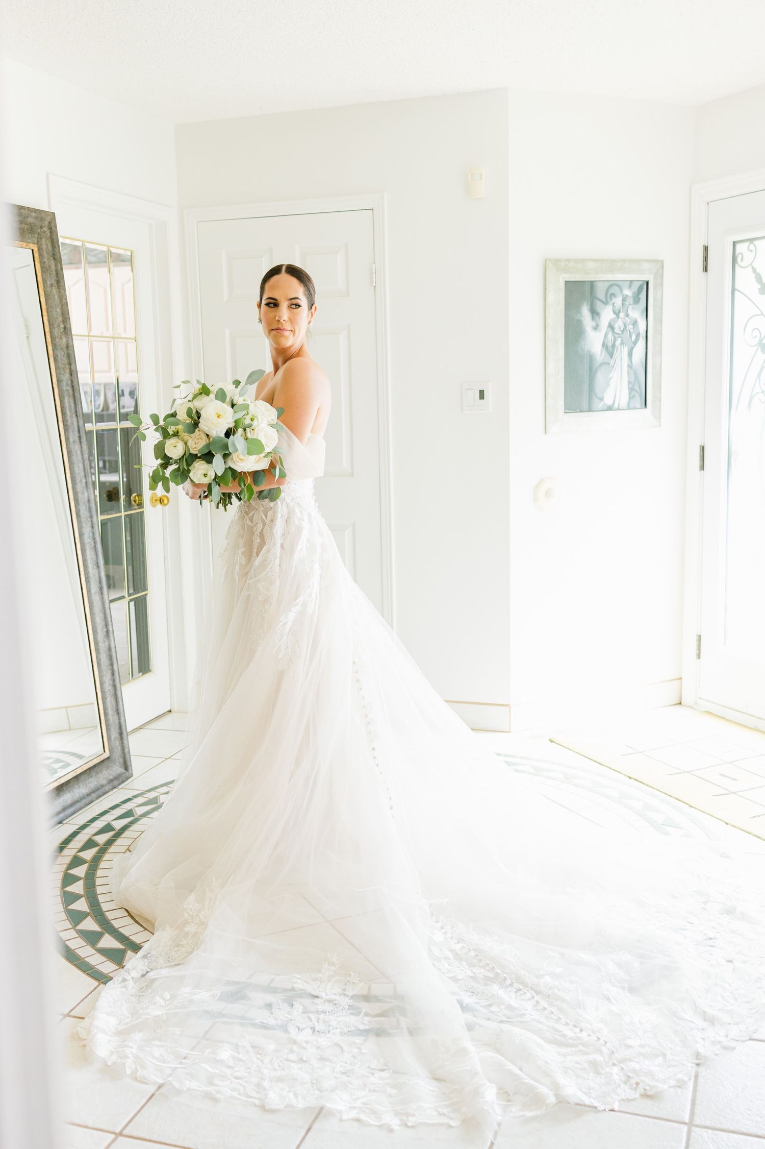 Elegant bridal portrait in flowing white gown with long train in bright sunlit room.