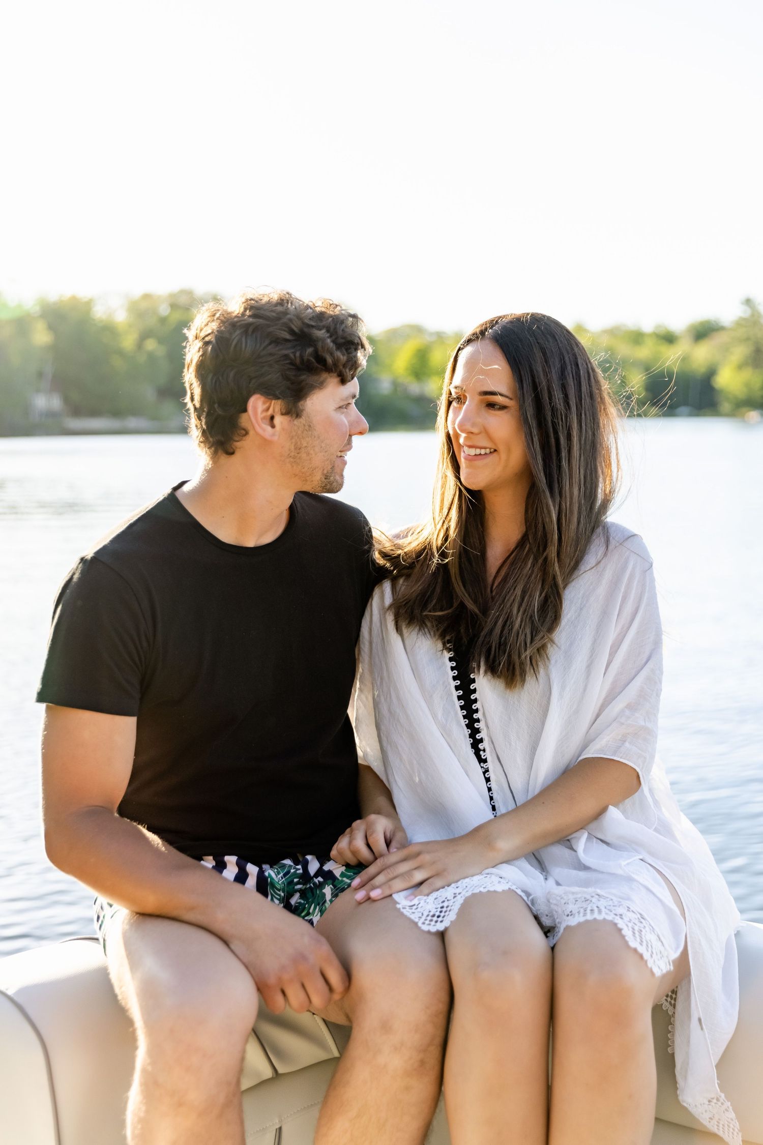 Happy couple in casual summer wear sharing laughs while sitting on boat cushions by the lake.