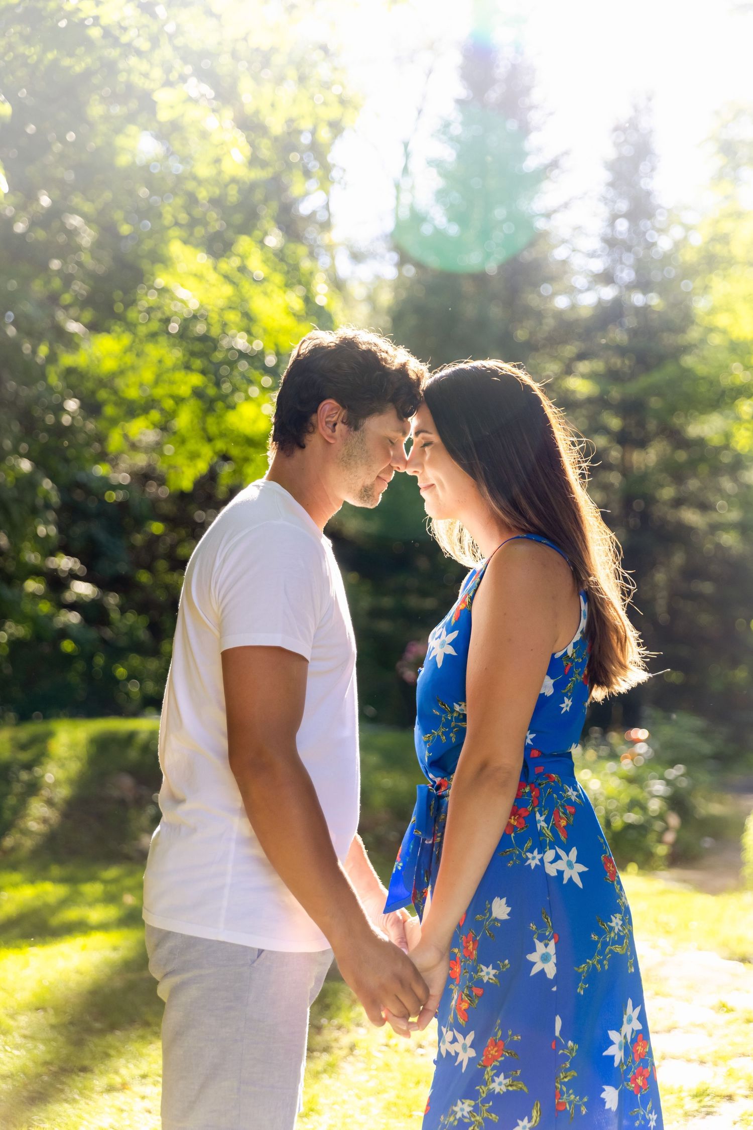 Couple in white and blue outfits sharing an intimate moment in a sun-drenched forest setting.