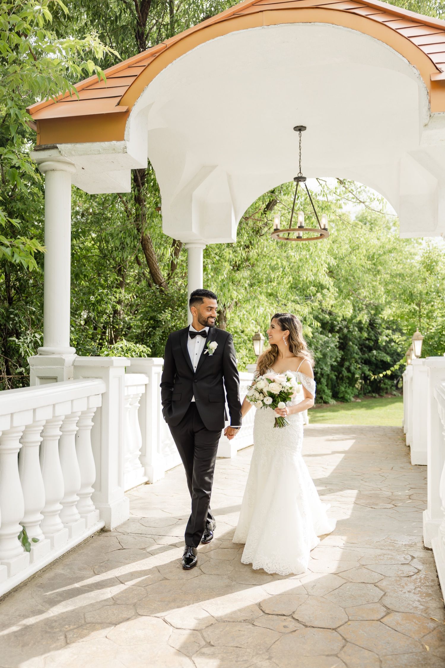 Stylish couple walks hand in hand under elegant covered walkway with hanging chandelier.