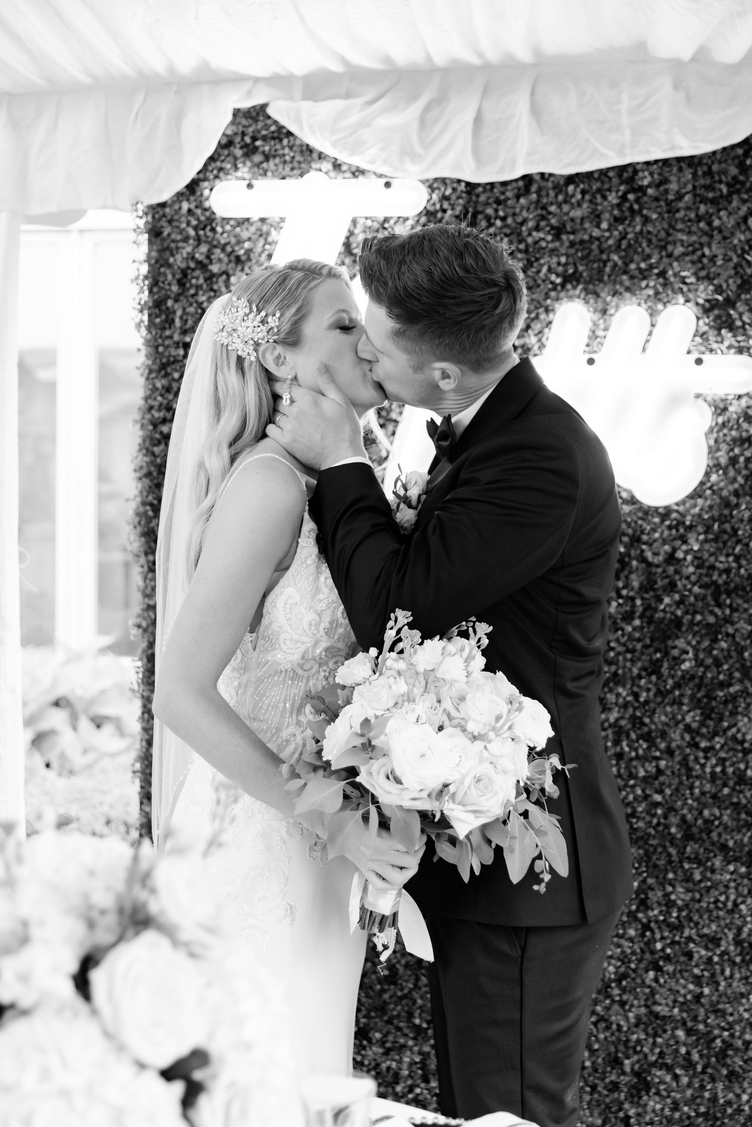 Black and white wedding portrait with floral backdrop.