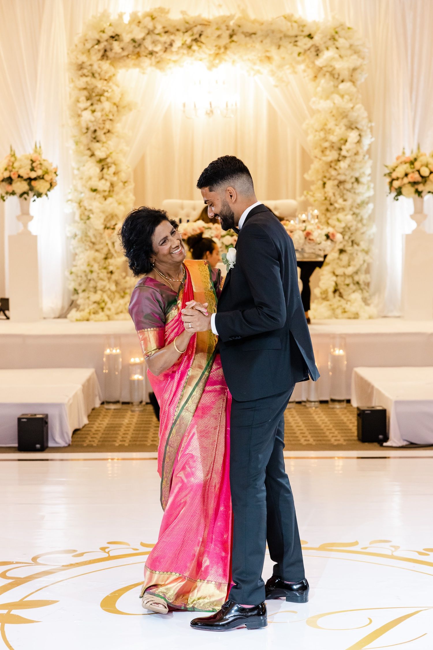 Couple shares an intimate dance moment under a cream floral arch at their wedding reception.