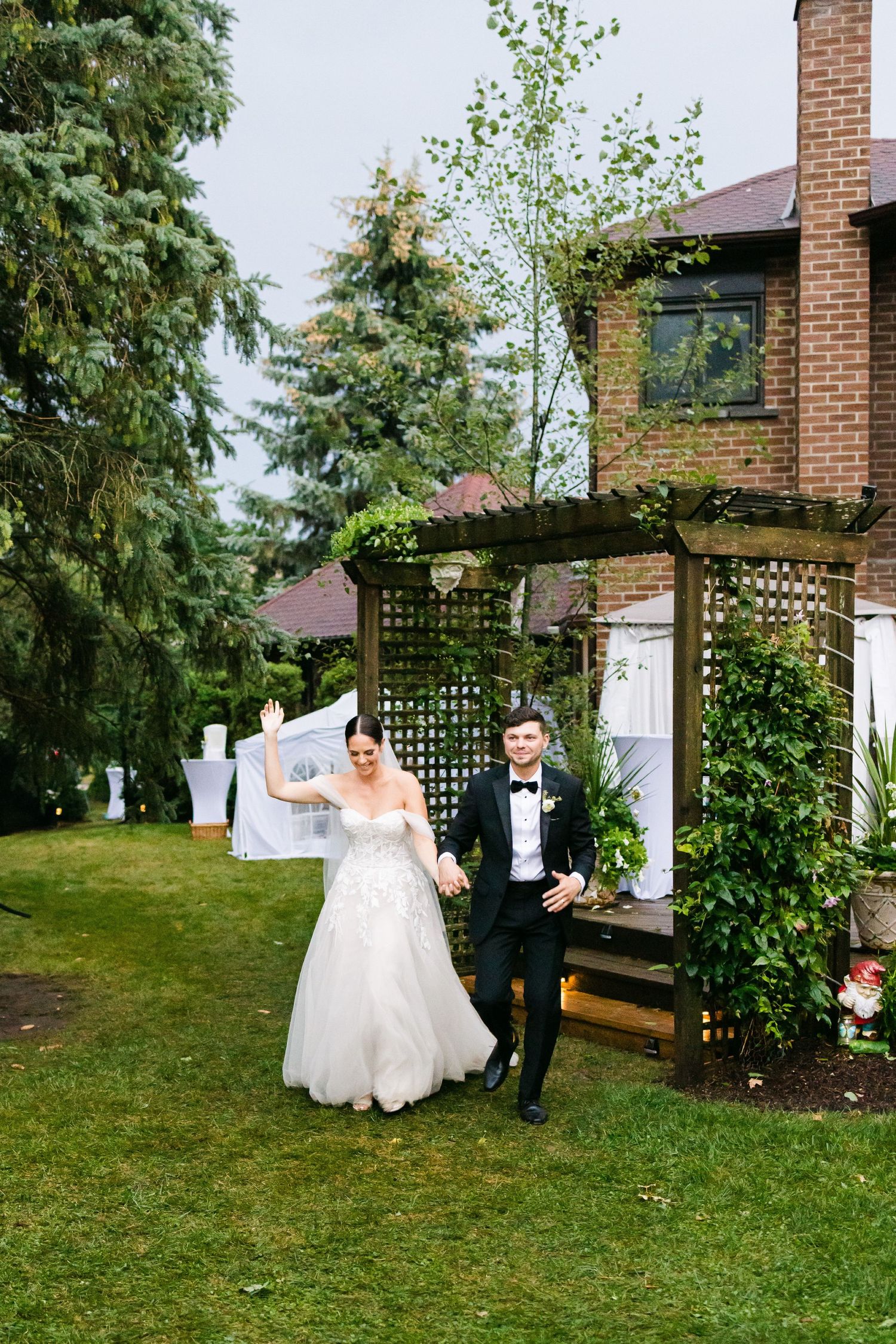 Wedding couple poses outside brick house with lattice garden trellis and evergreen landscaping.