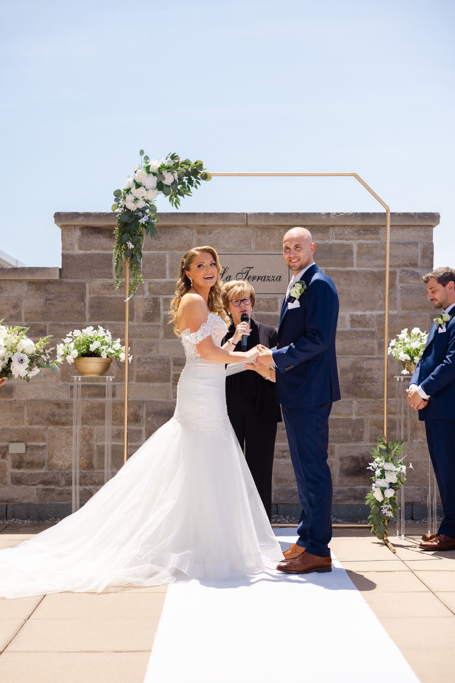An intimate wedding ceremony on a rooftop patio with a geometric arch decorated with white flowers.