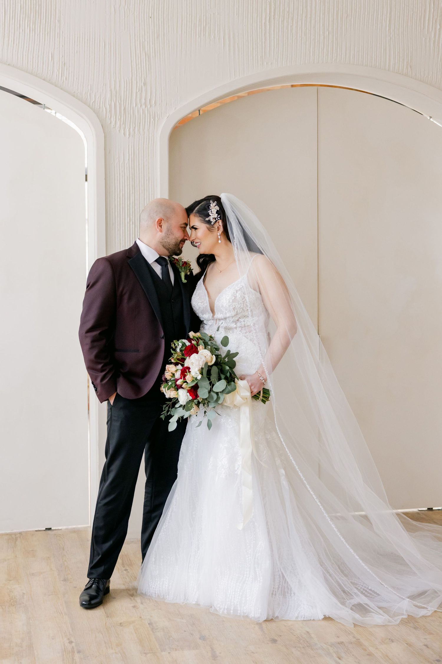 Romantic wedding portrait under white archways with flowing bridal veil.