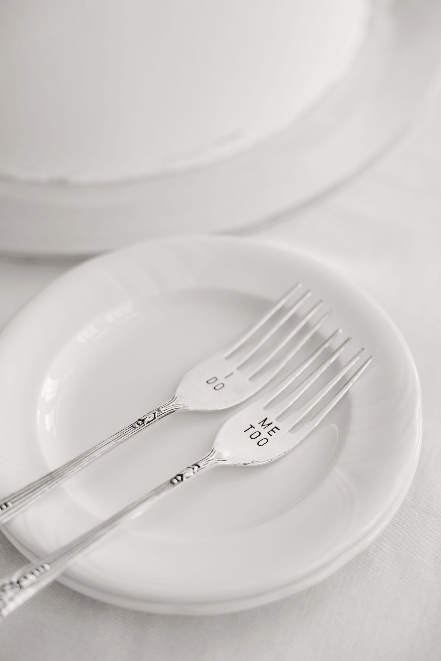 Two silver forks placed on a white plate against a light background.