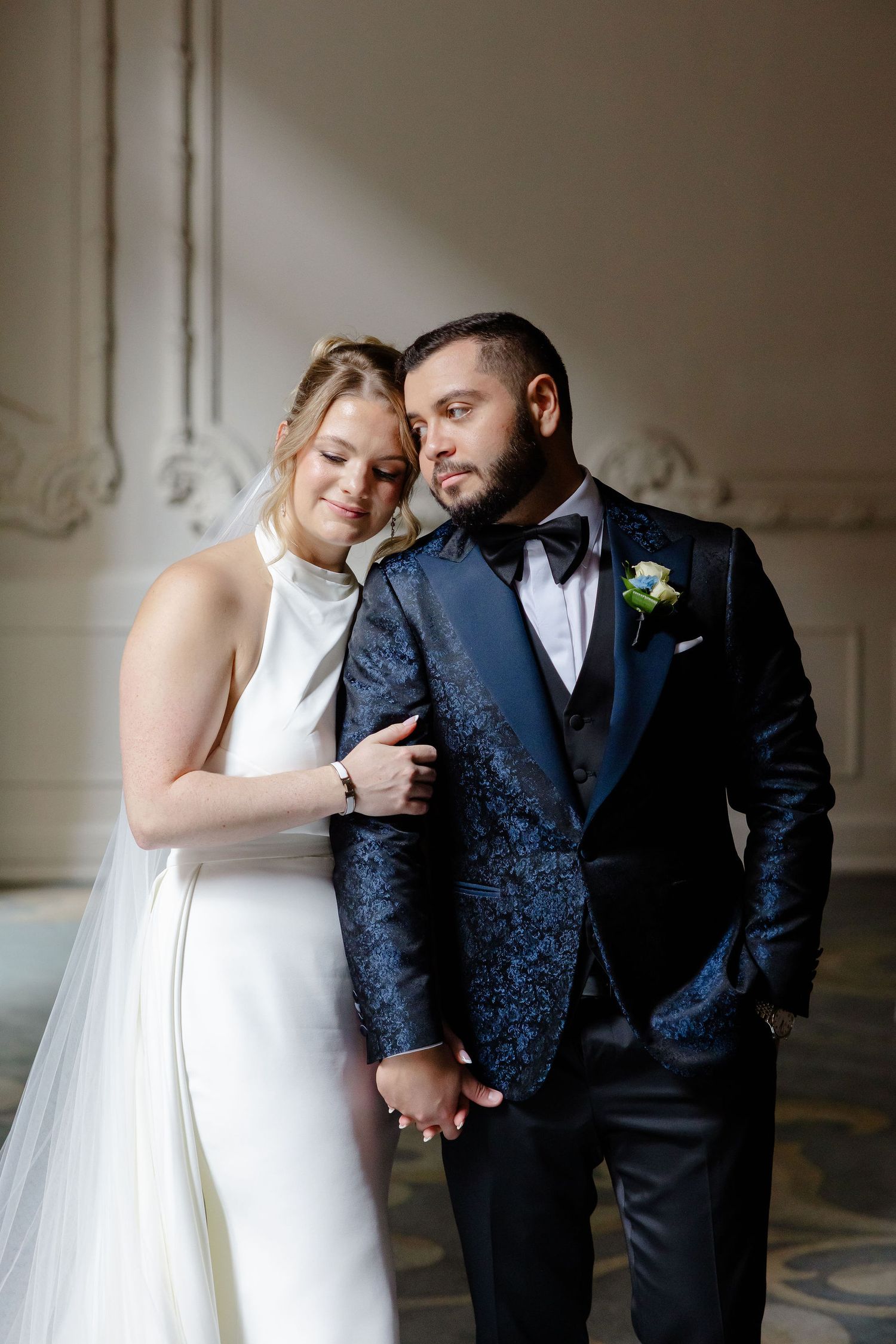 A romantic wedding couple poses together in a classic indoor setting wearing formal attire.