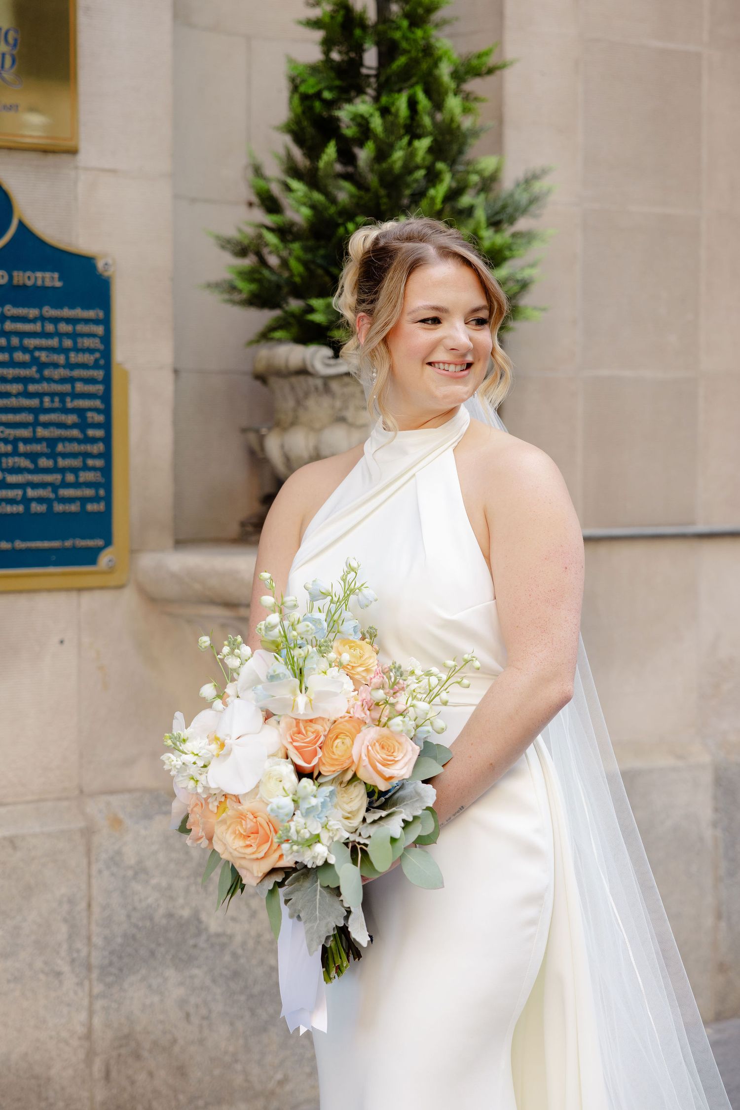 Elegant bridal portrait showcasing peach and white floral bouquet against stone wall.