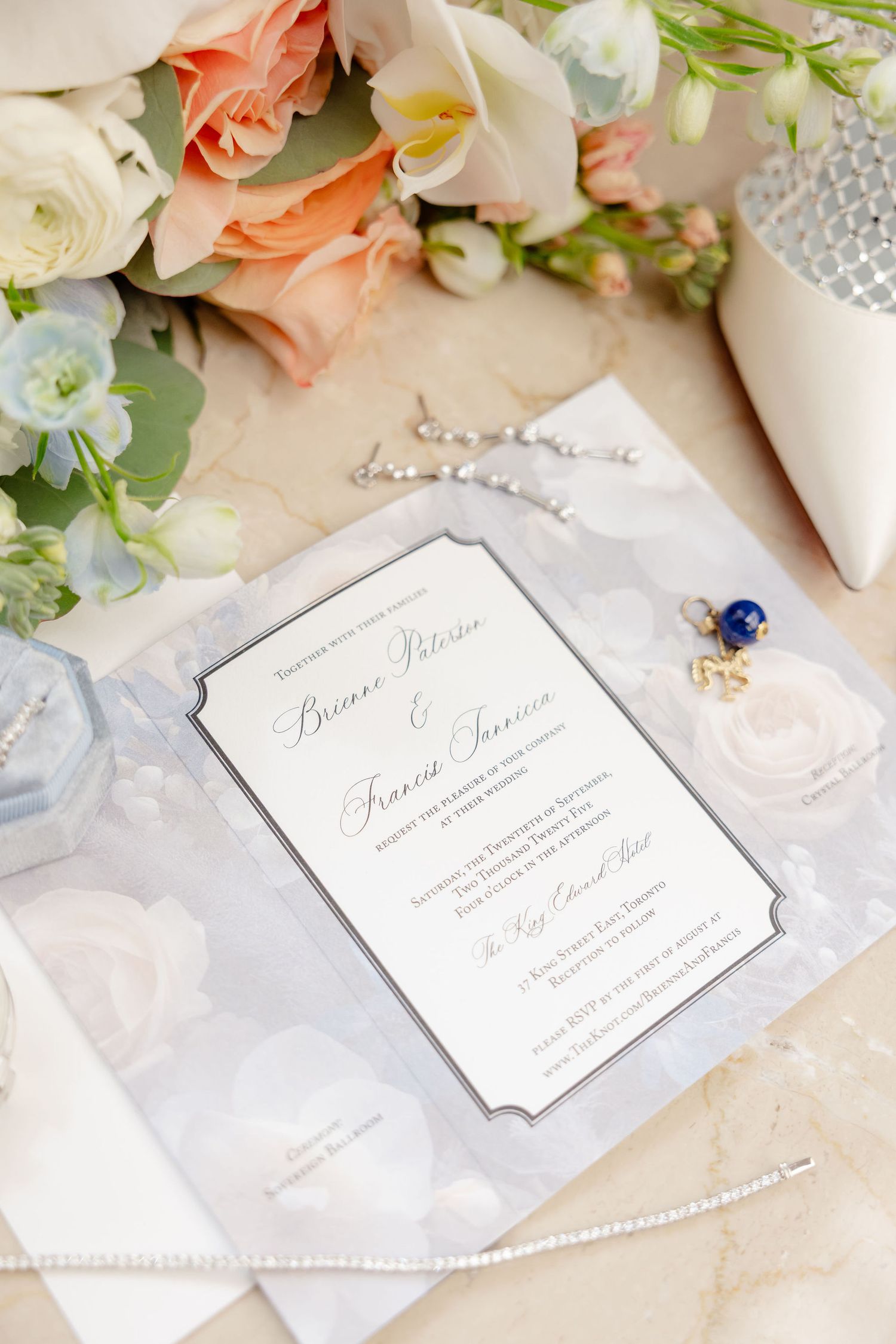Elegant wedding invitation with peach and white flowers, pearls, and delicate details on a light background.