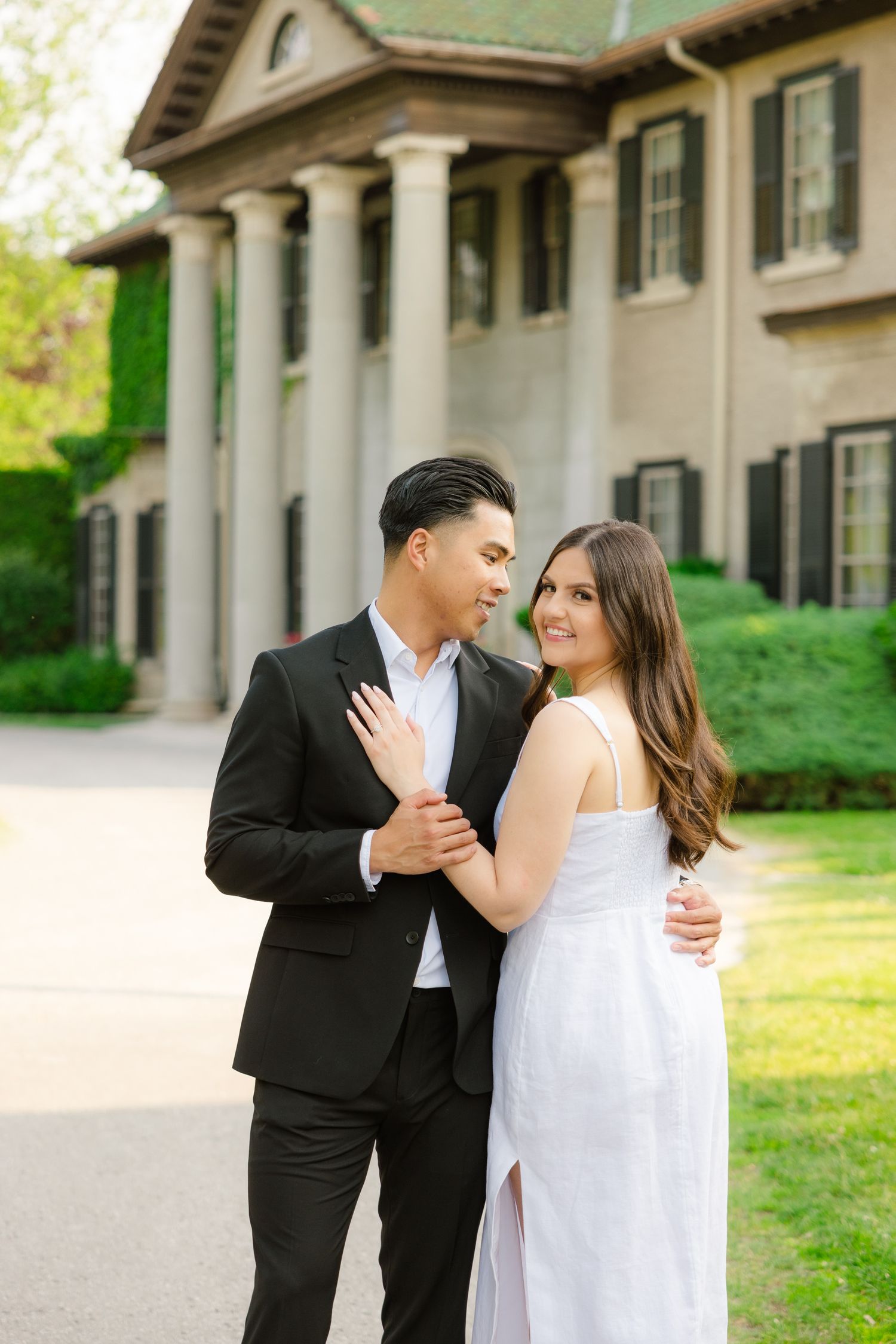 Romantic couple poses in formal attire outside an elegant colonial mansion with white columns.