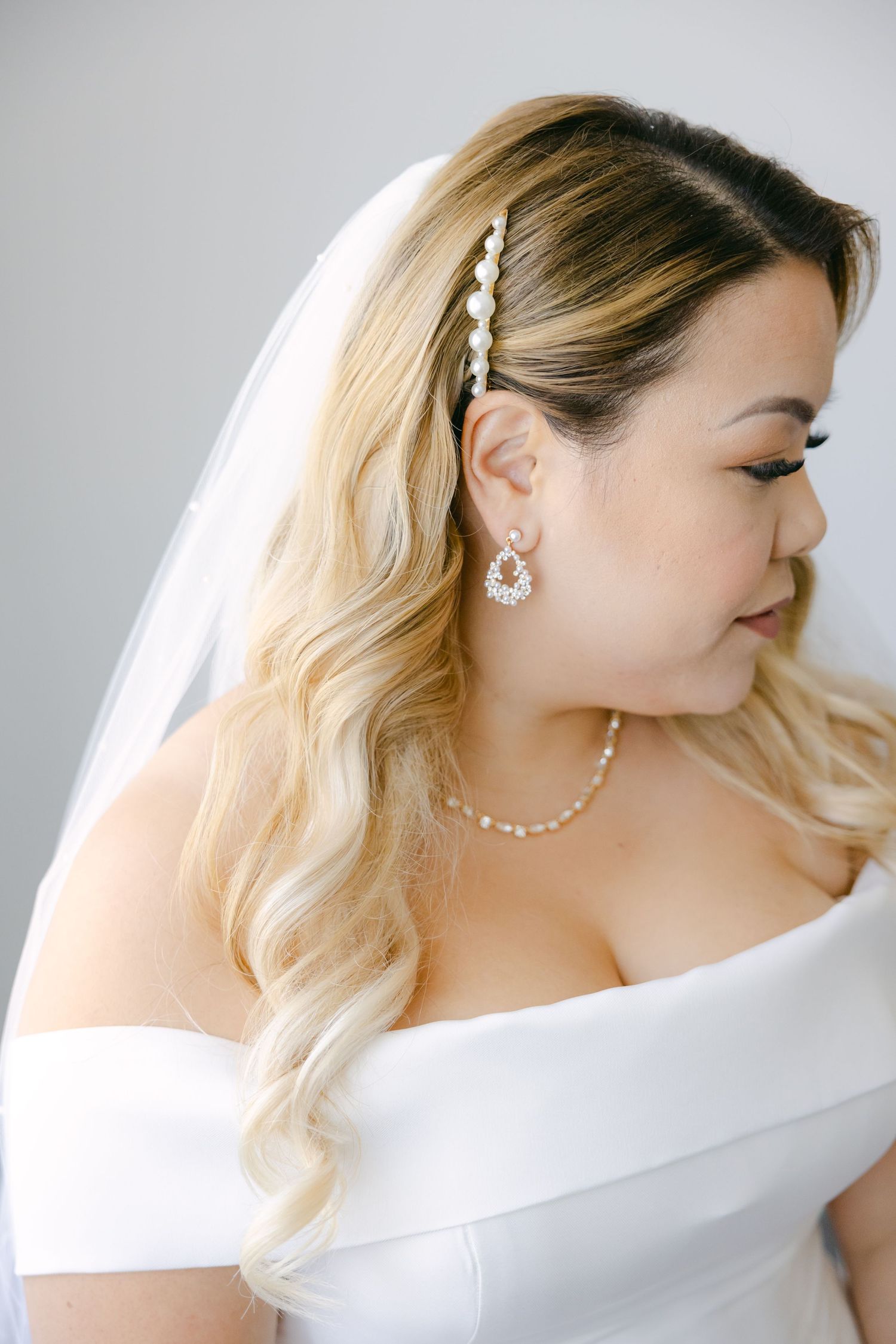 Close-up of bridal accessories including pearl hair clip, earrings and delicate necklace.