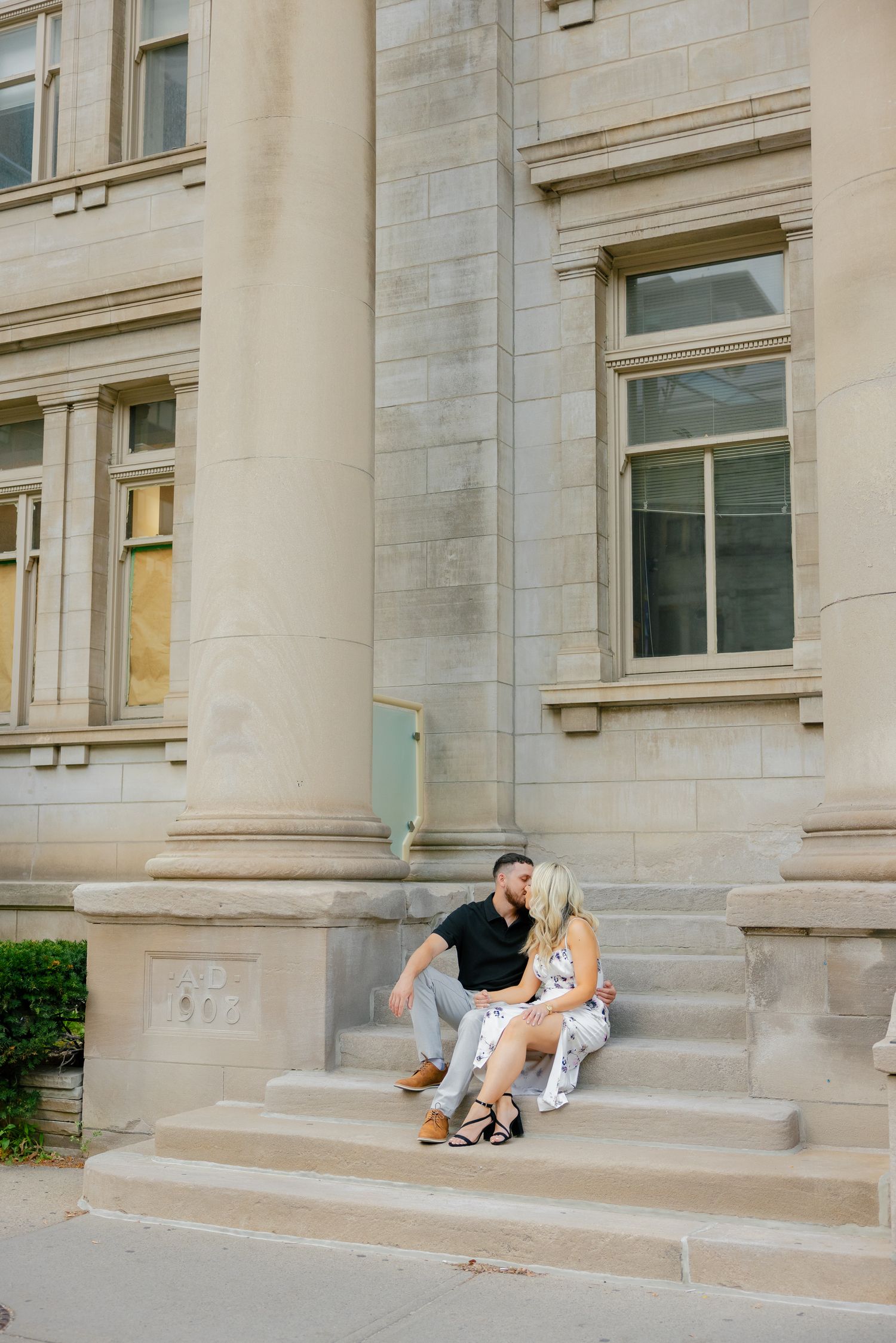 A couple shares an intimate moment while seated on exterior building steps.