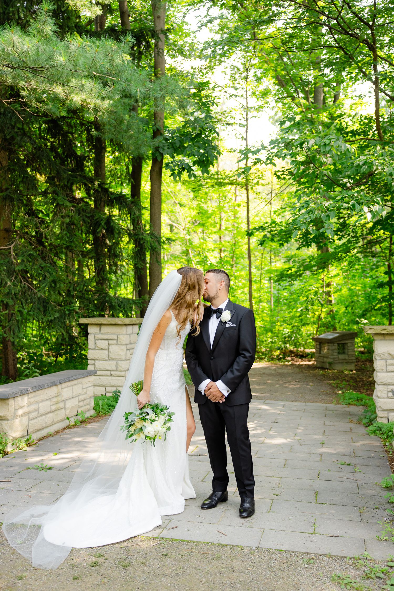 Wedding couple shares romantic moment on garden path with lush greenery backdrop.