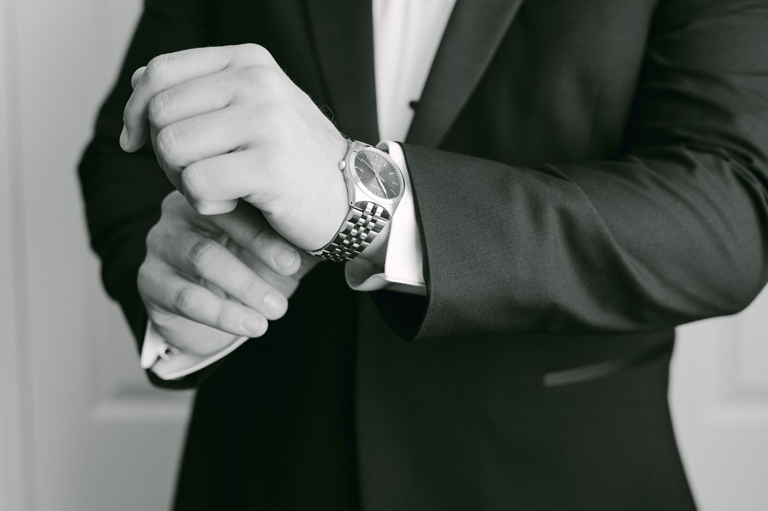 Close-up detail shot of hands adjusting a silver watch while wearing a formal black tuxedo.