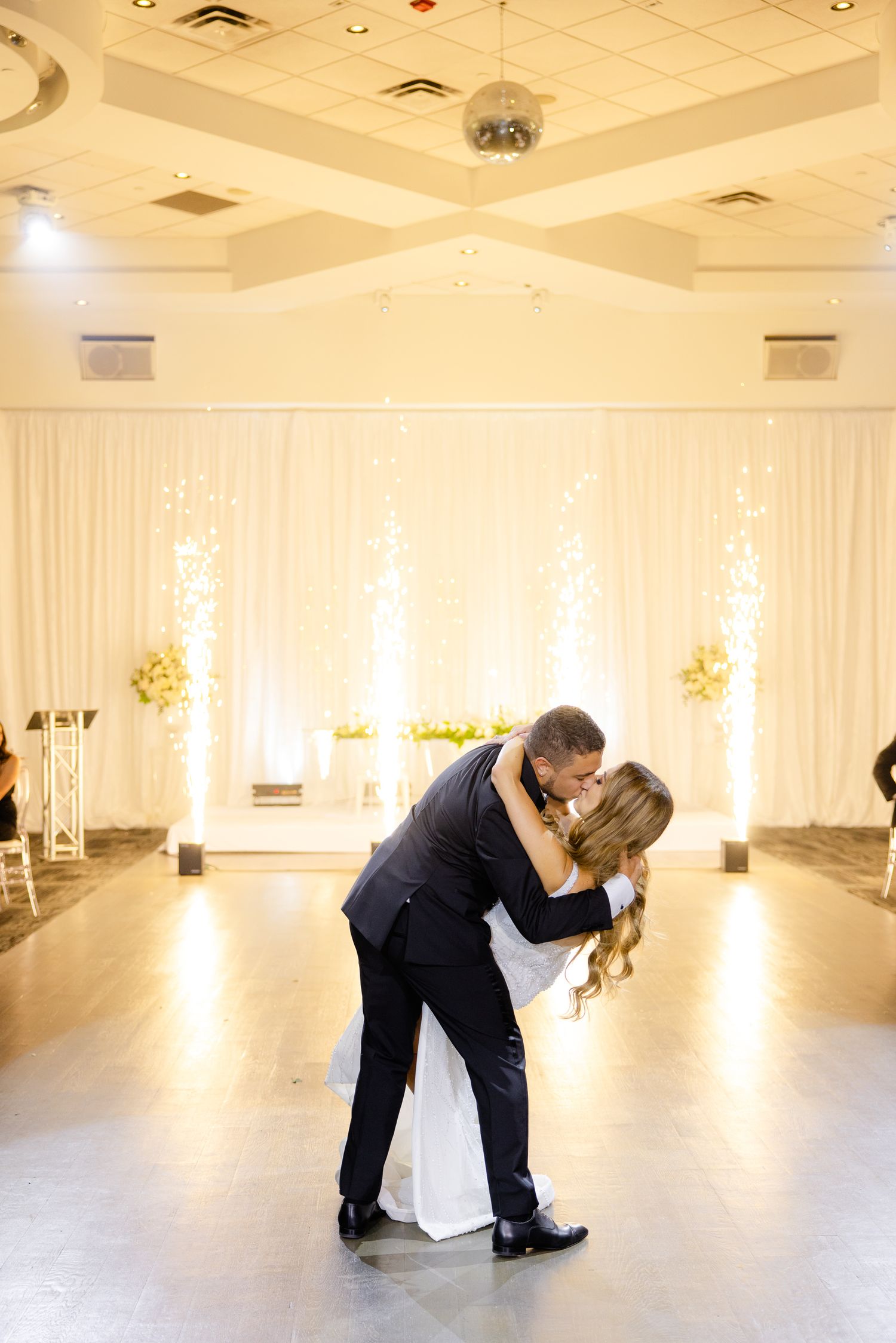 Romantic dance dip in an elegantly decorated wedding venue with white draping and ambient lighting.