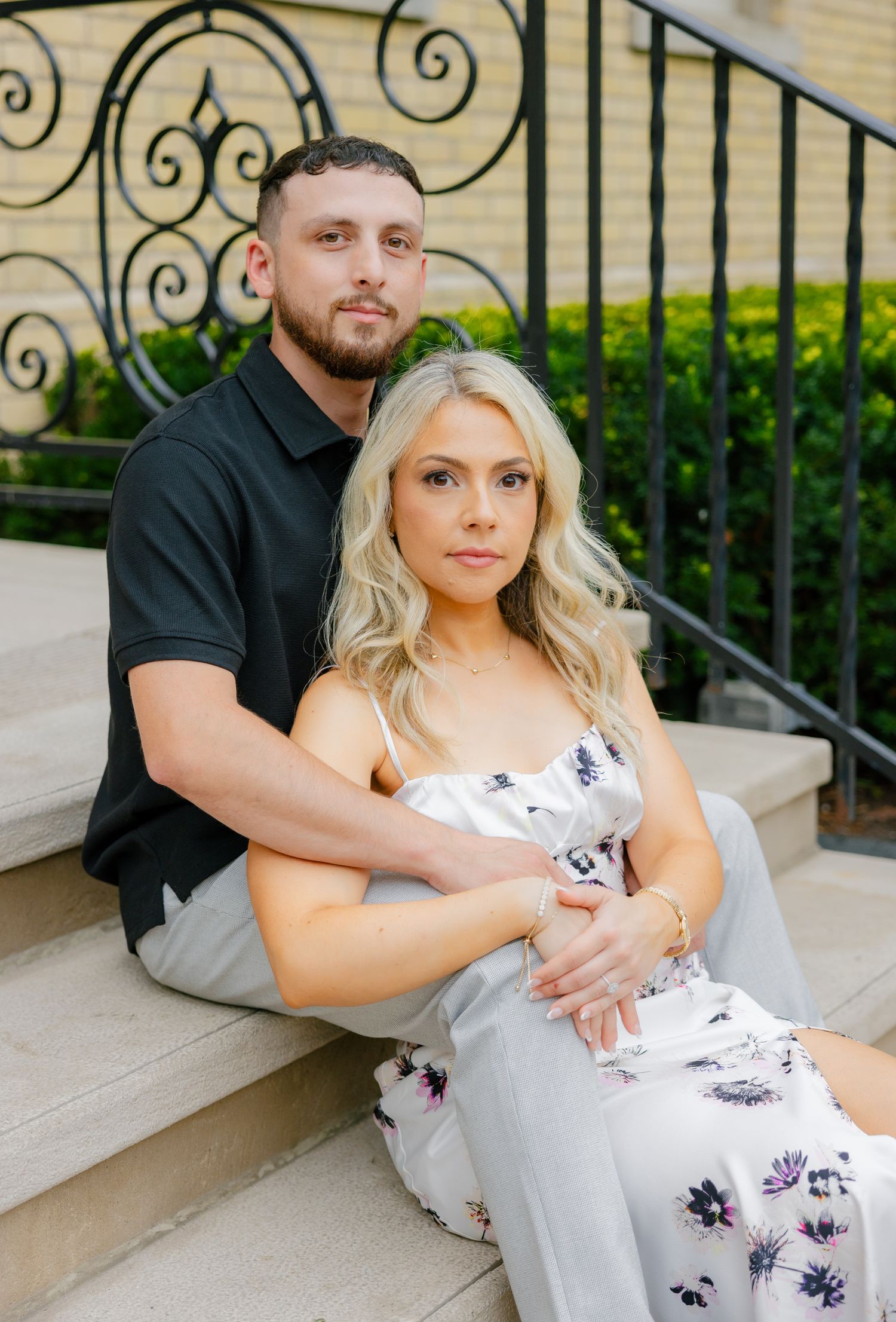 An intimate portrait of a couple embracing on stone steps with ornamental iron railings.