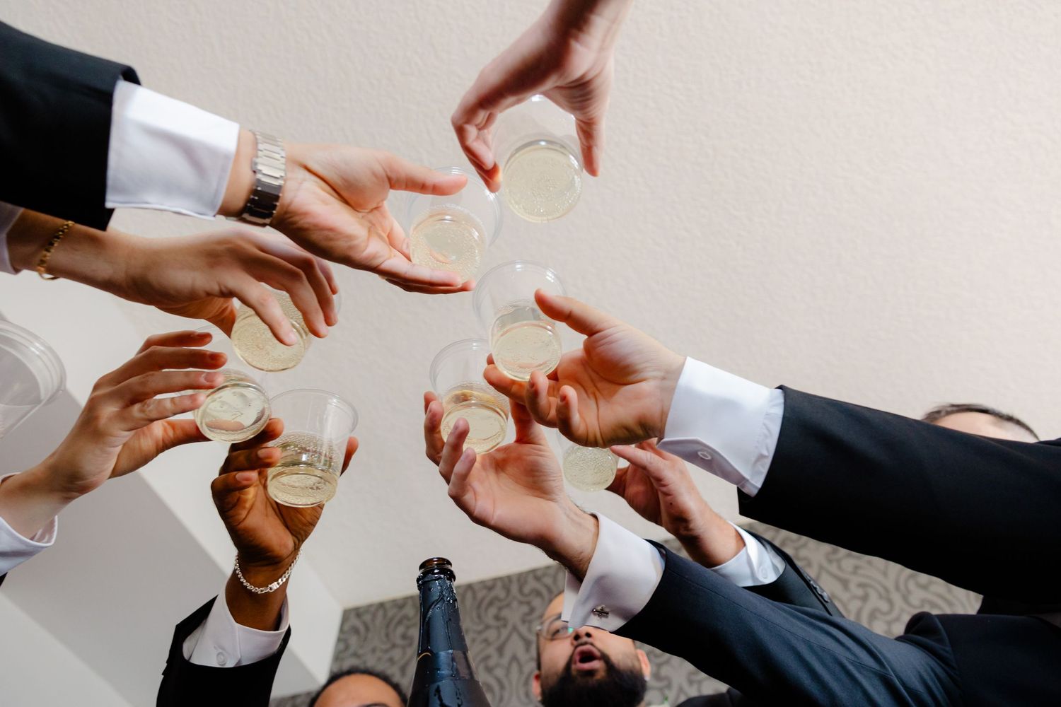 Hands in formal suits reaching in to toast with glasses in a circle formation.