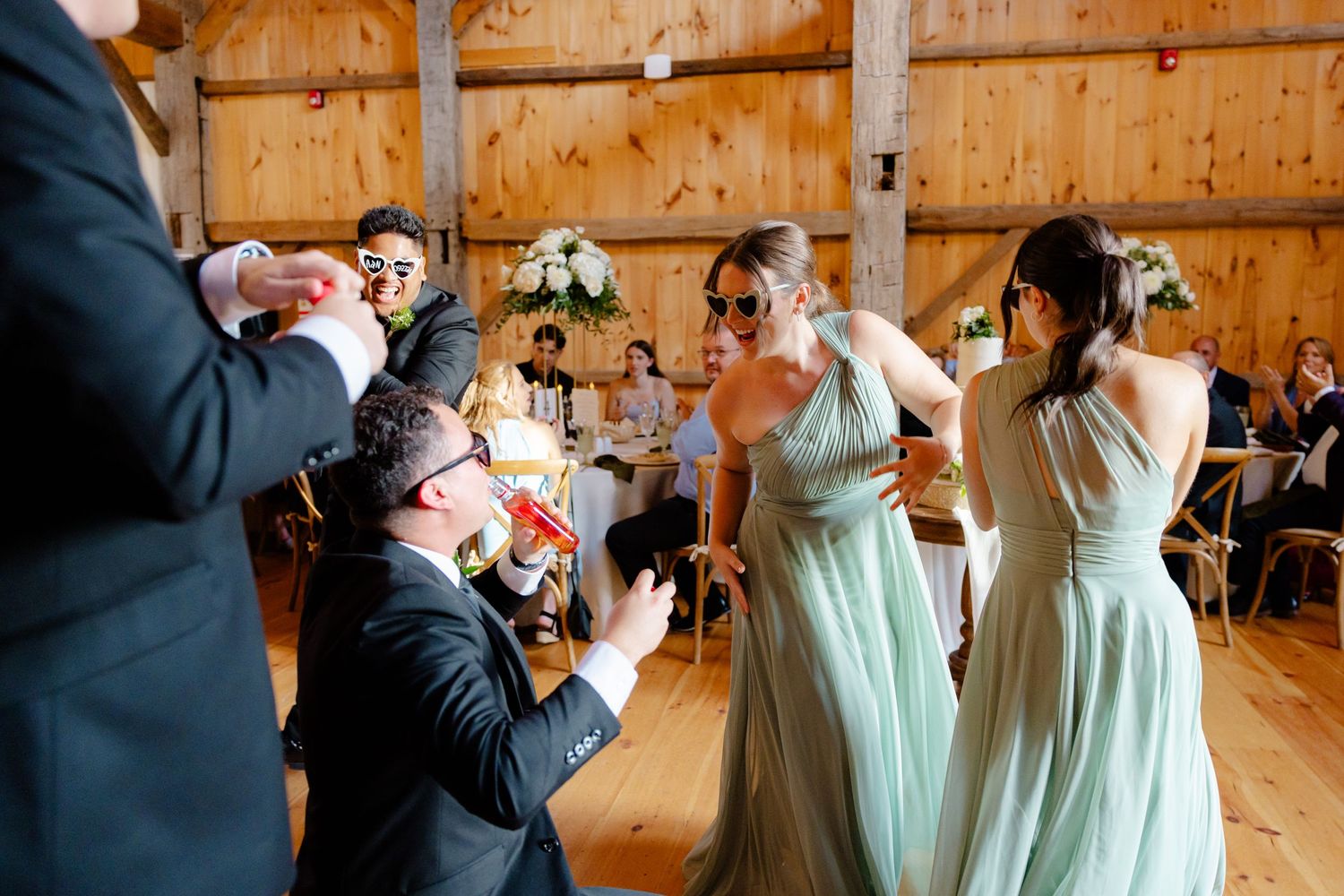 Wedding party members toast and celebrate in a rustic barn setting.