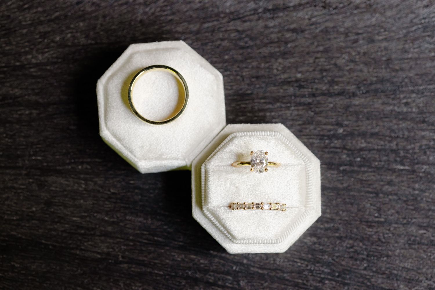 Two octagonal white ring boxes containing wedding bands and engagement rings on dark surface.