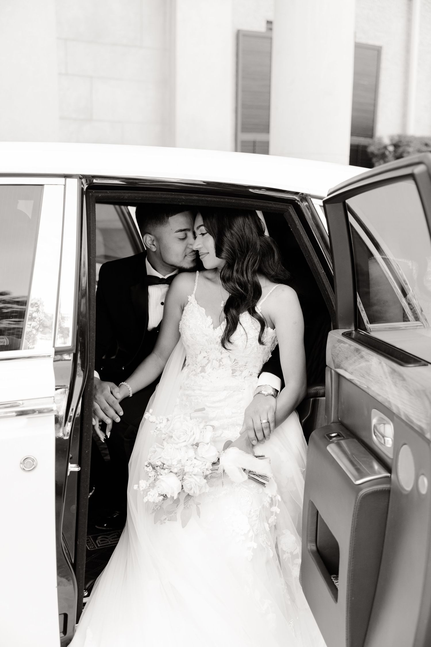 Black and white photo of newlyweds sharing an intimate moment in a luxury car.