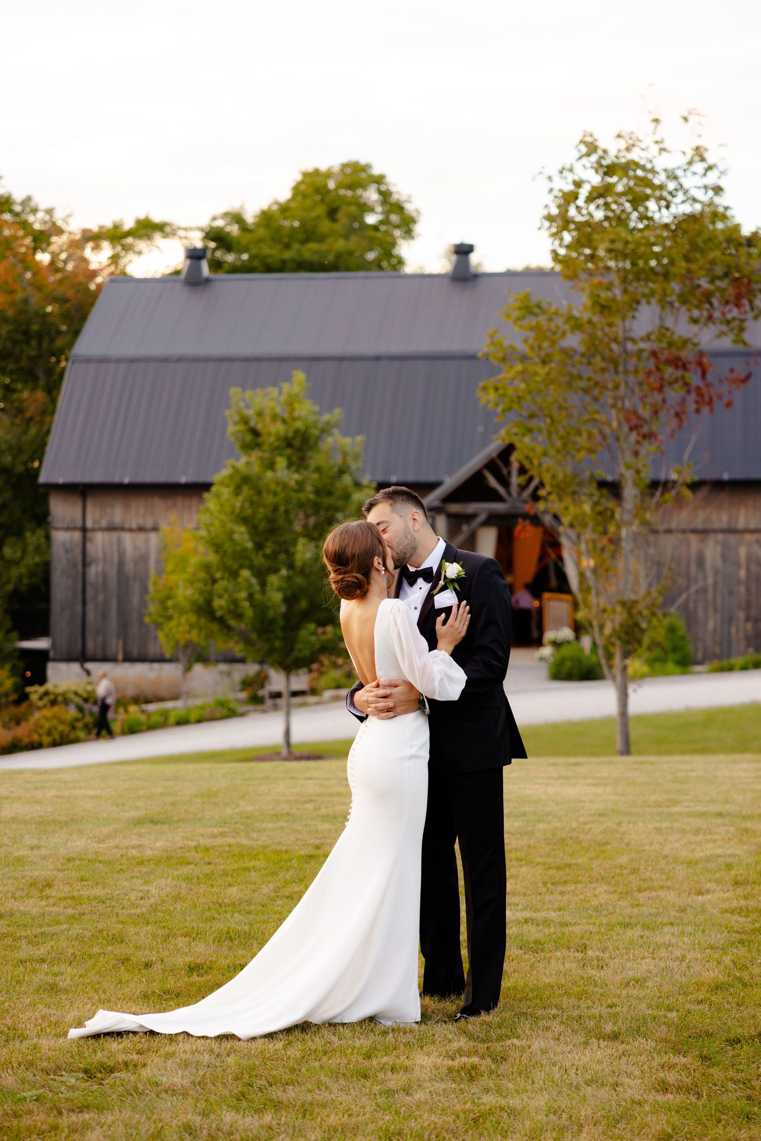 A romantic embrace between newlyweds on a lawn with a barn venue in the background.