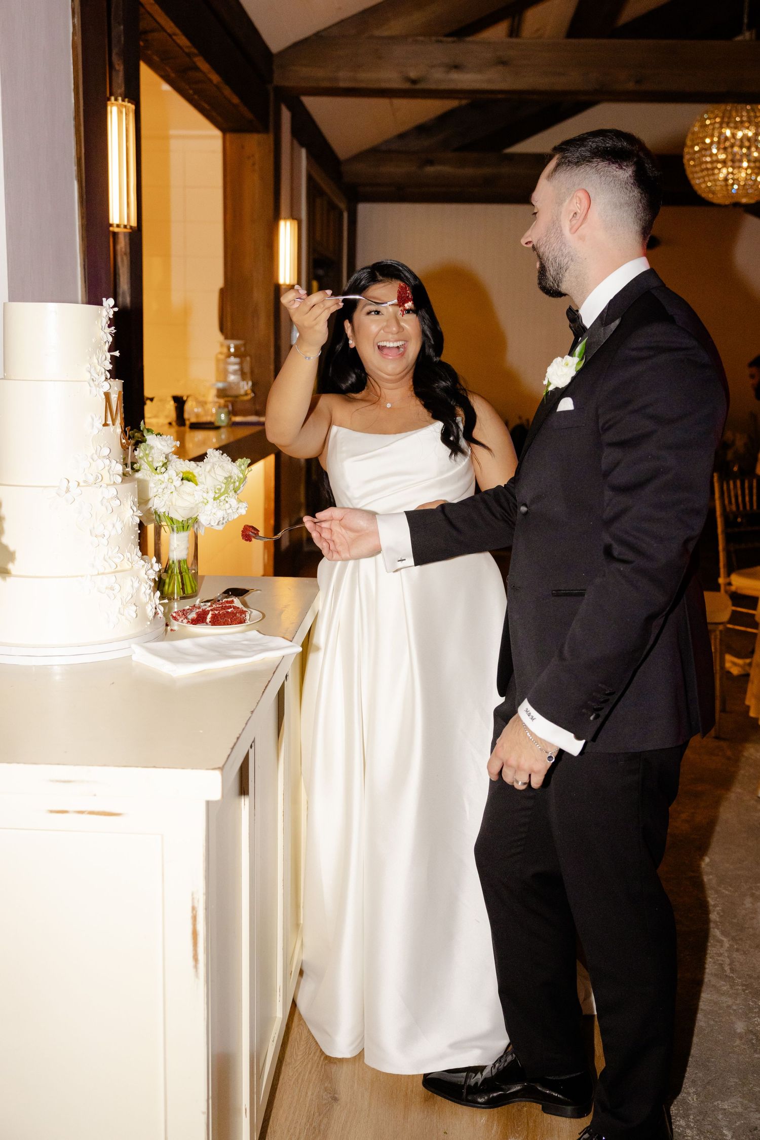 Wedding celebration moment by the cake as couple share joyful reactions in elegant wedding attire.
