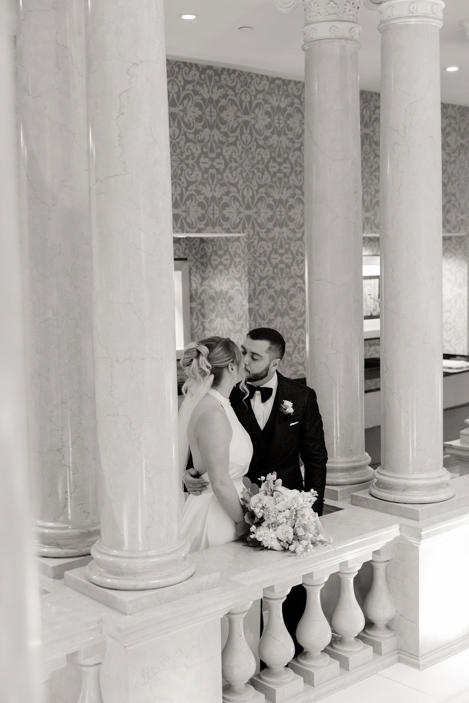 Wedding couple posing between classic white columns in an elegant venue interior.