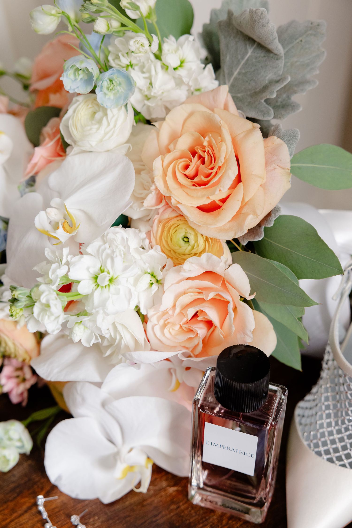 Wedding details featuring peach roses, white flowers and a glass perfume bottle arranged artistically.
