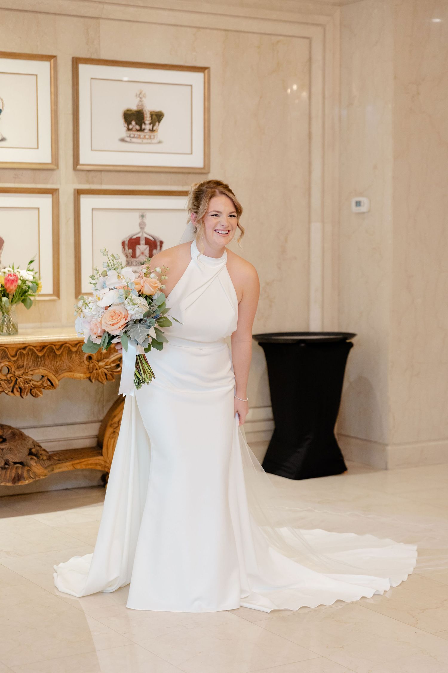 Bride in elegant white gown poses with flowing train in luxurious indoor setting.