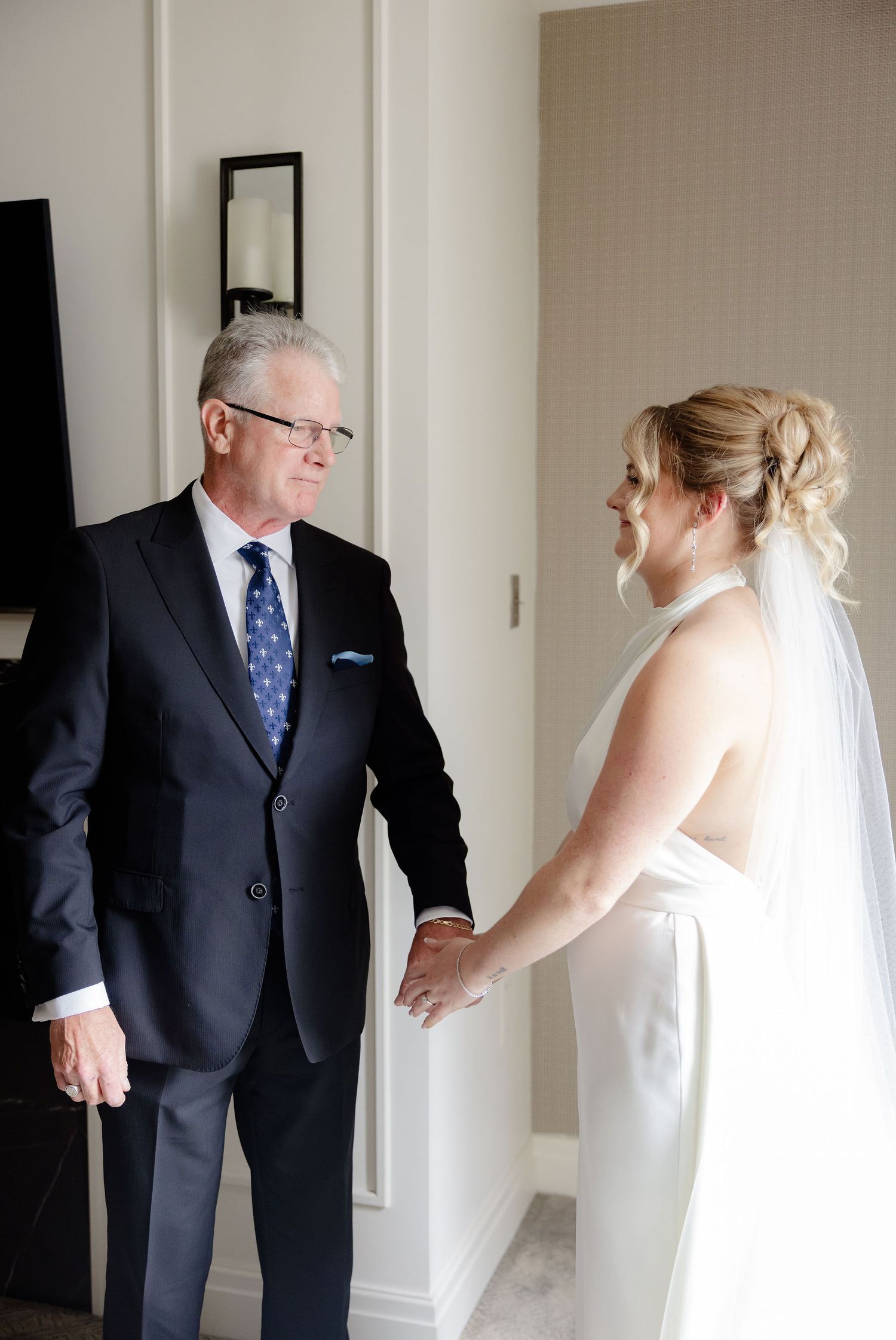 An emotional reveal between a bride in white and someone in a dark suit in a light-colored hallway.