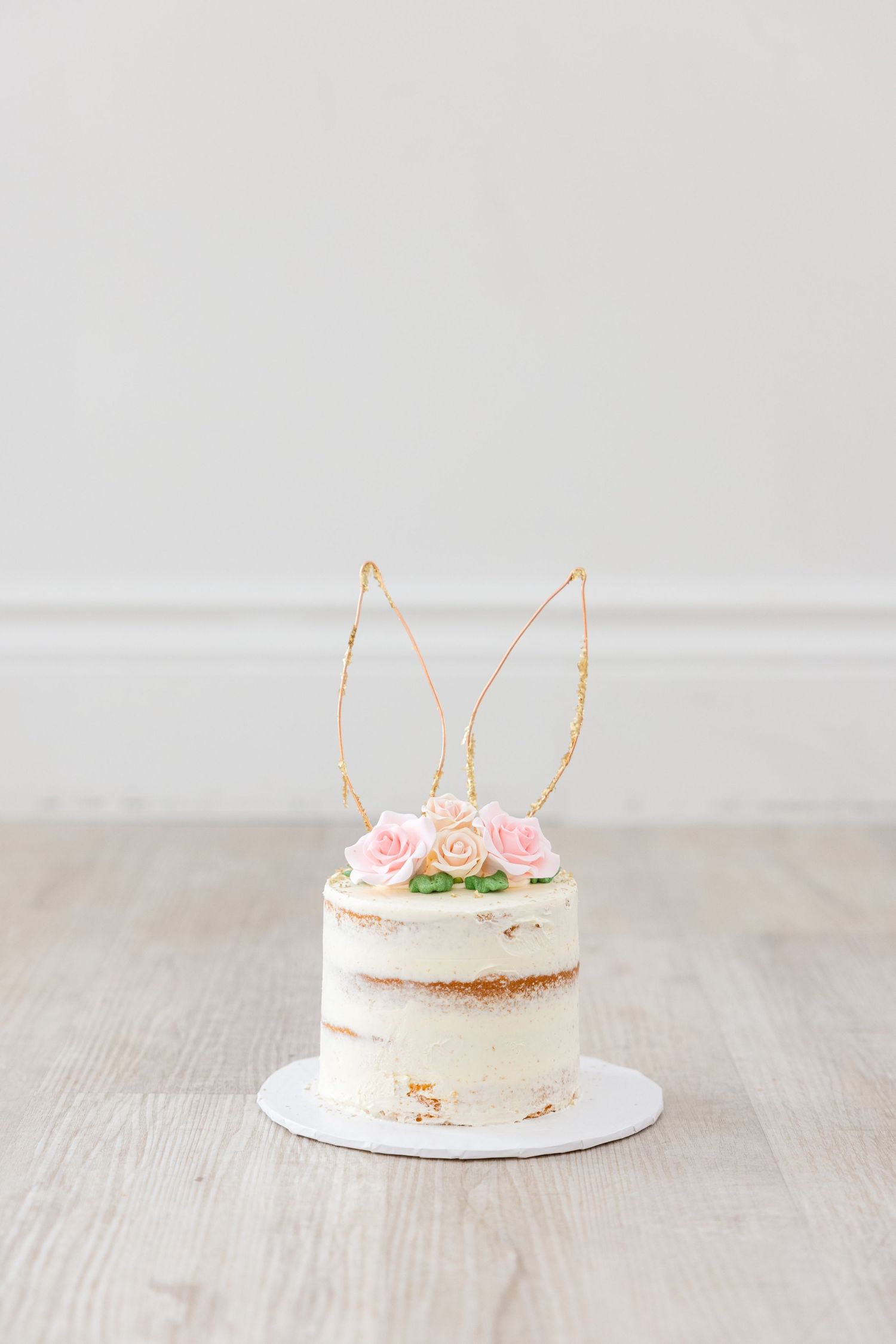 Simple naked cake decorated with pink roses and gold wire bunny ears on top.