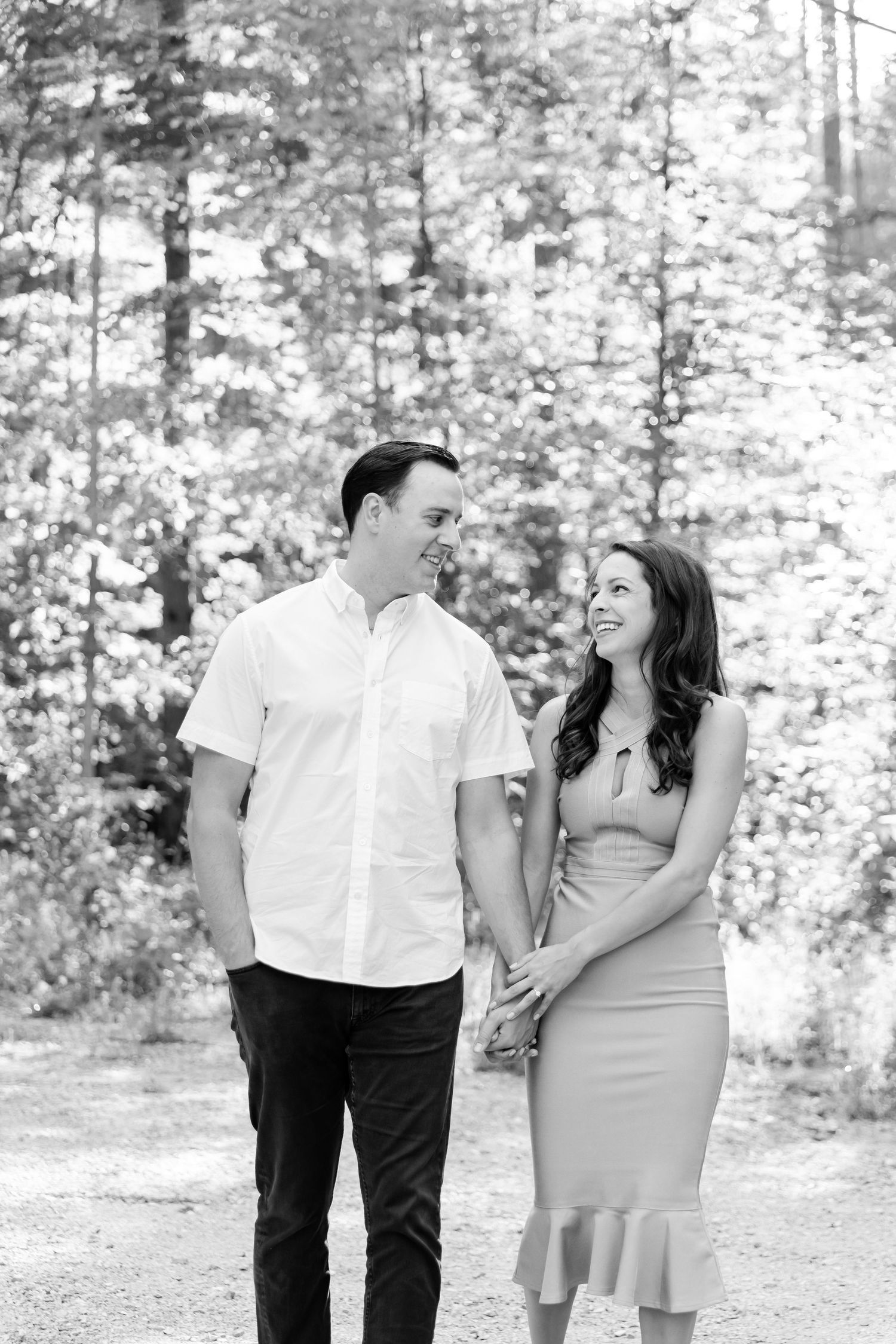 Black and white portrait of a couple holding hands and smiling on a forest path.