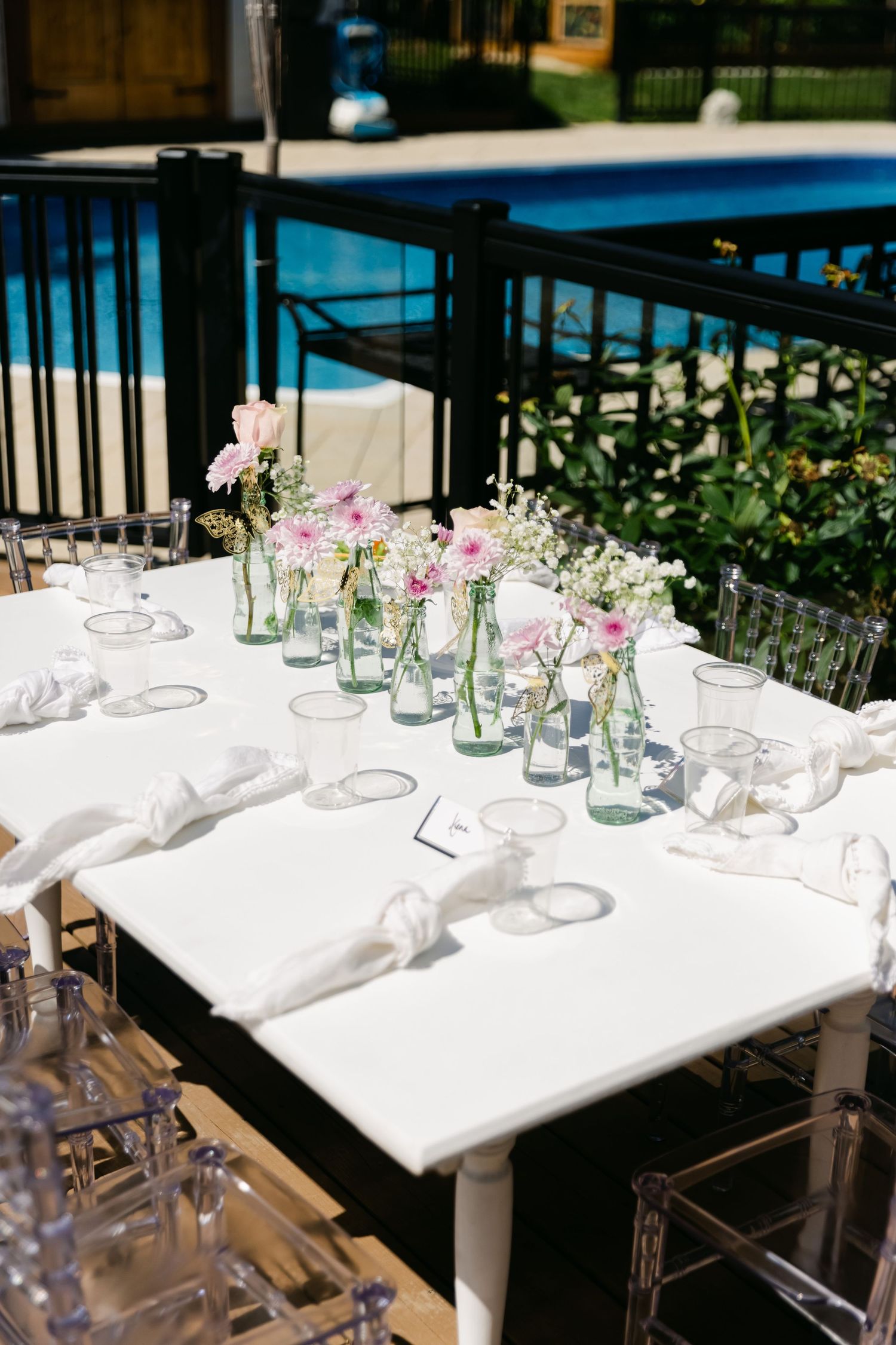 Elegant outdoor table setting with row of glass vases containing delicate pink and white flowers.